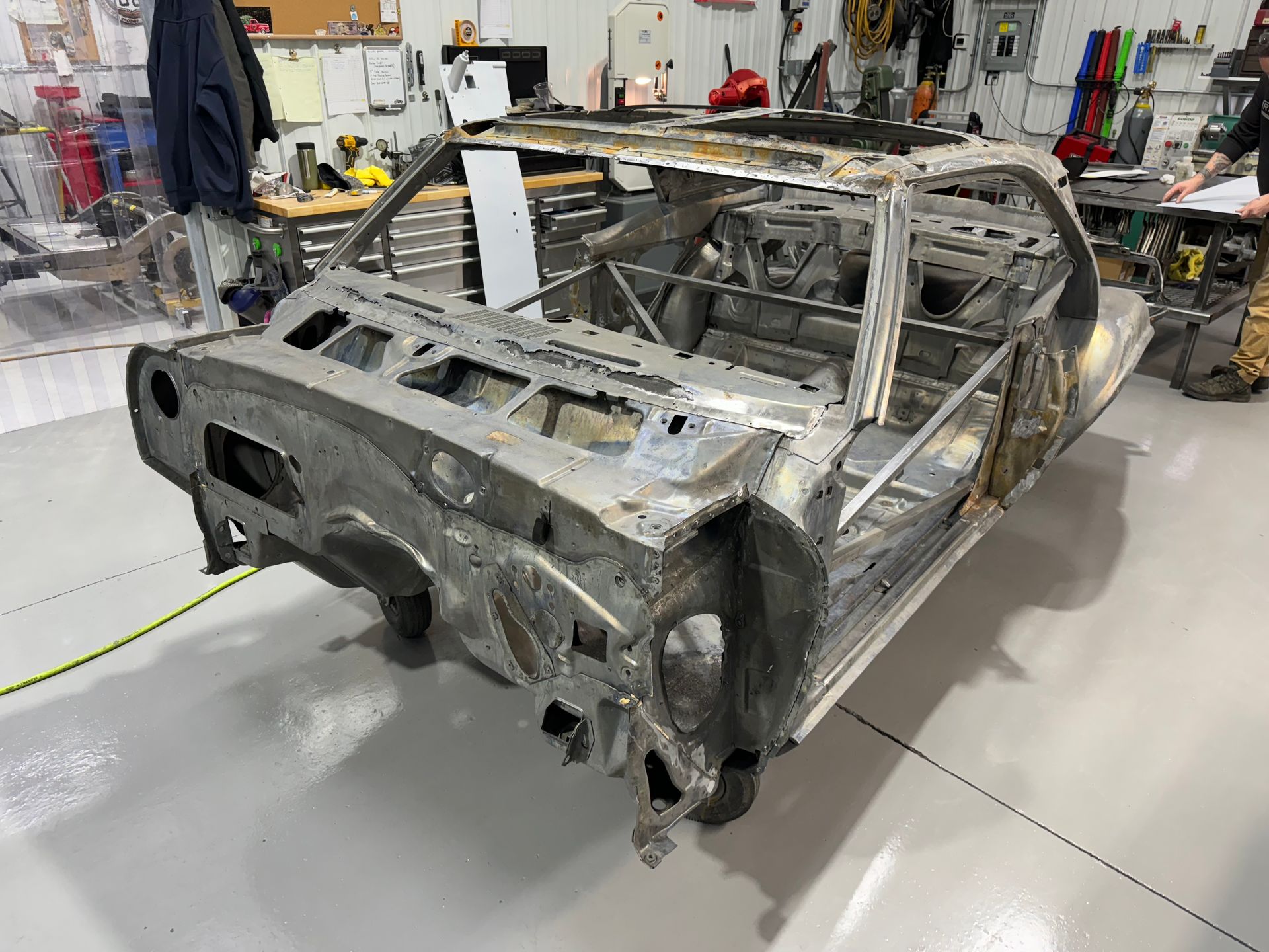 Stripped car chassis in a workshop, with exposed metal frame and missing body panels.
