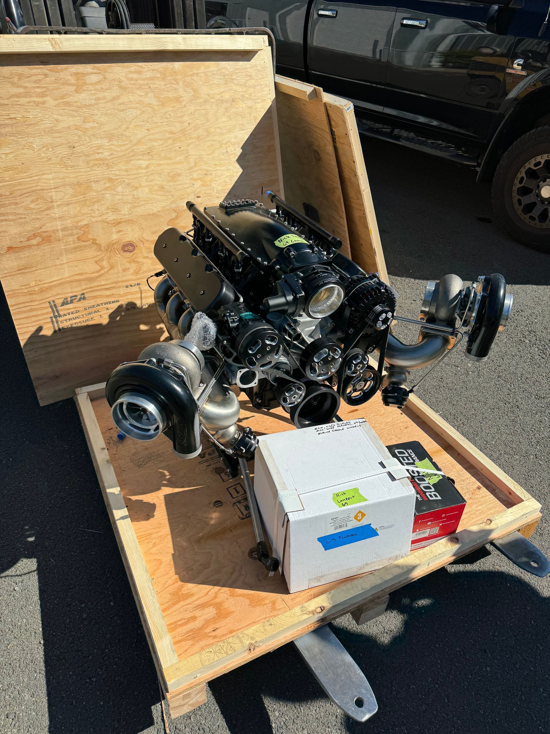 Engine and turbo assembly strapped inside a wooden crate on a trailer outdoors.
