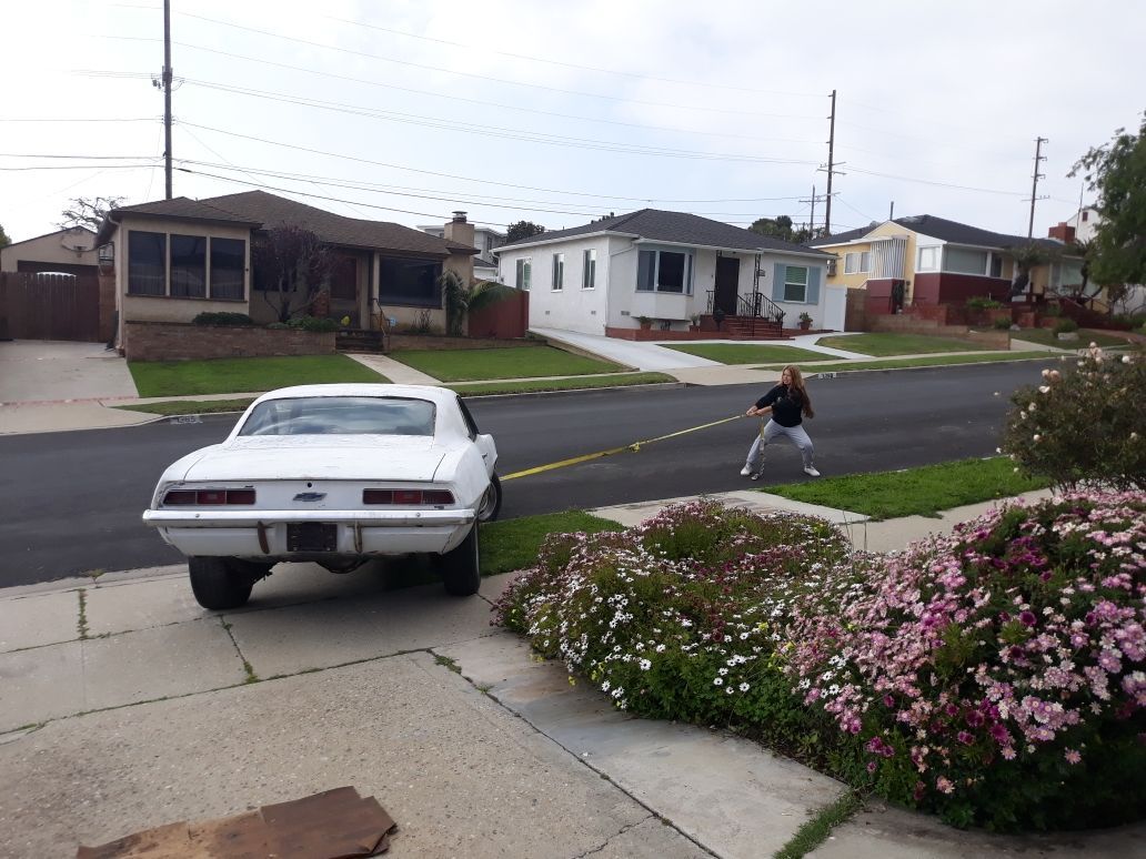 Person on sidewalk pulling a white car with a rope in a suburban street.