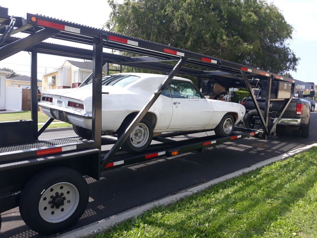 White car on a flatbed trailer beside a parked truck on a residential street.