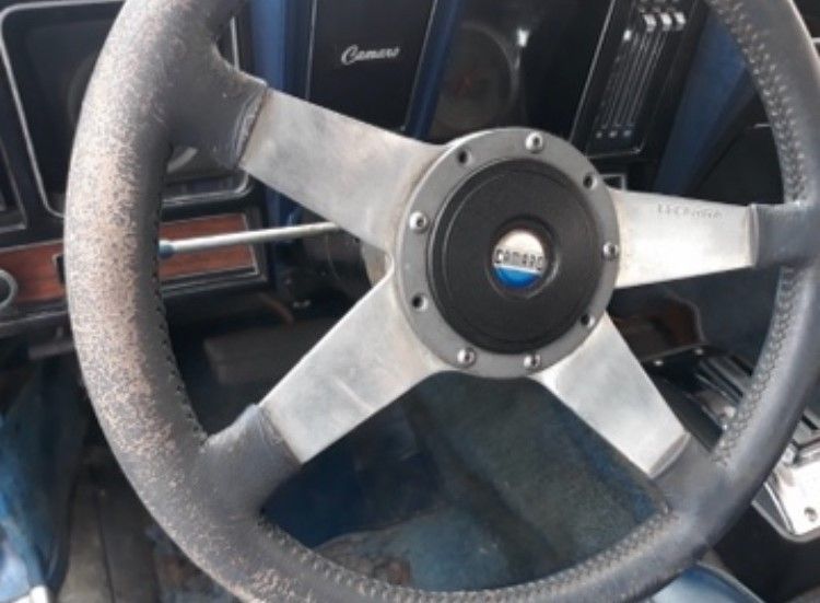 Close-up of a black three-spoke steering wheel with silver metal accents inside a vintage car interior