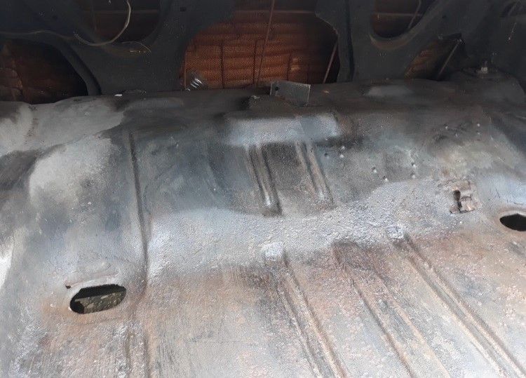 Rusty car trunk floor with worn metal panels and wheel wells exposed