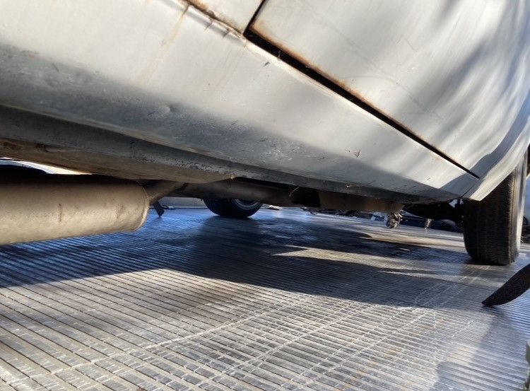 Undercarriage of a silver car on a metal ramp, with exhaust pipe and wheel visible.