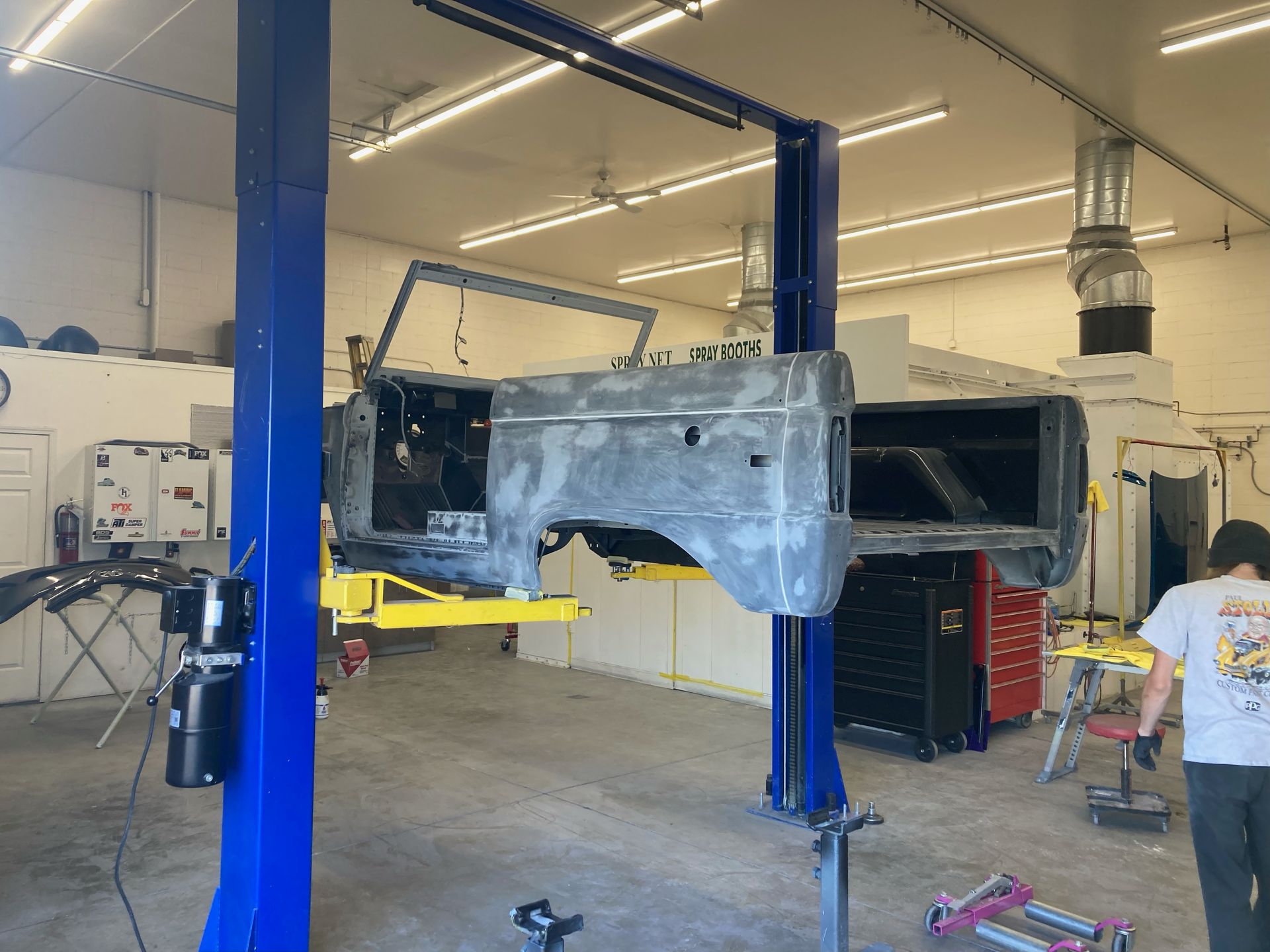 Car body suspended in a workshop on blue hydraulic lifts, with tools and equipment nearby.