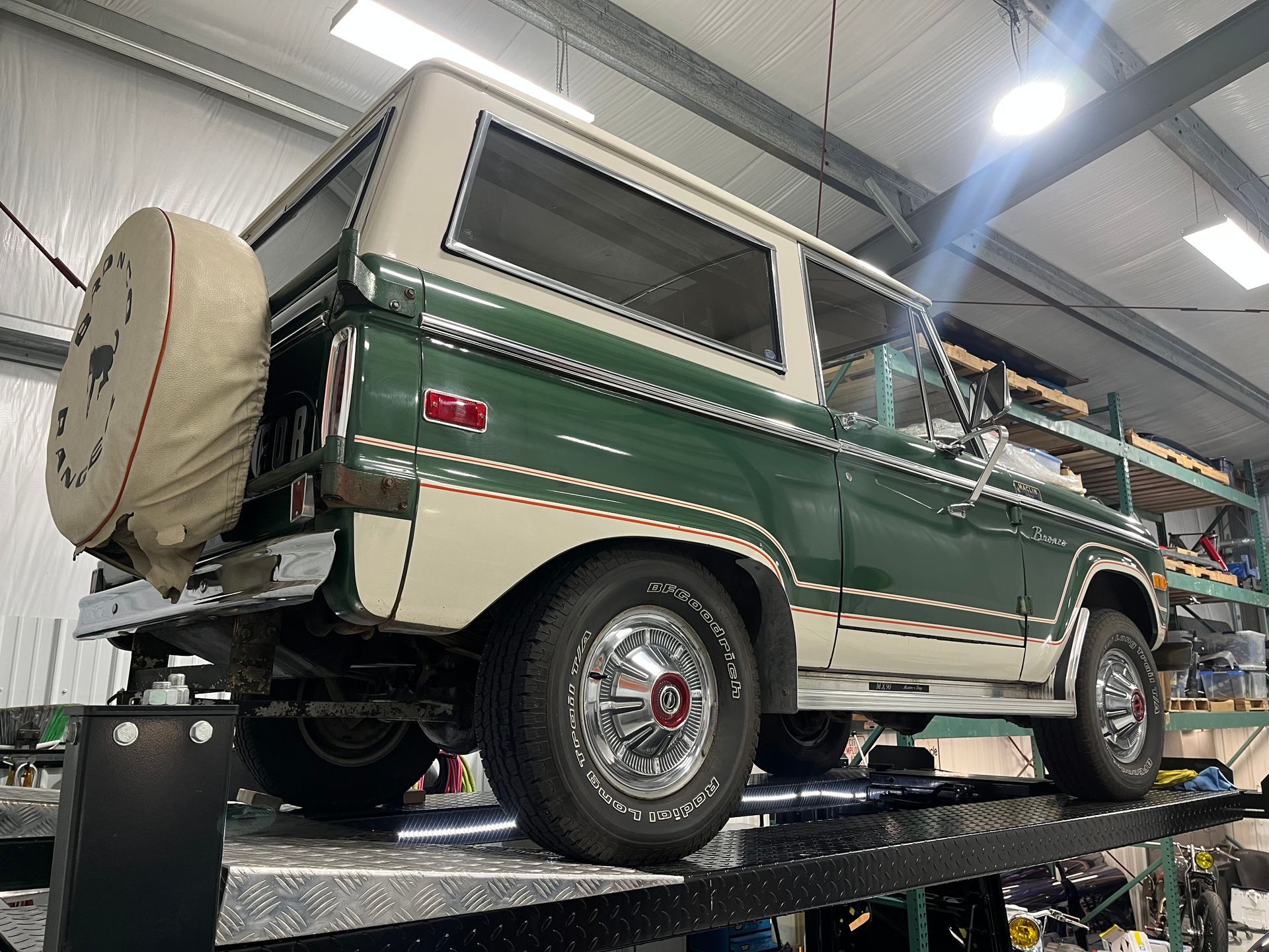 Classic green off-road SUV on a lift inside an auto shop, with a rear spare tire and white roof.