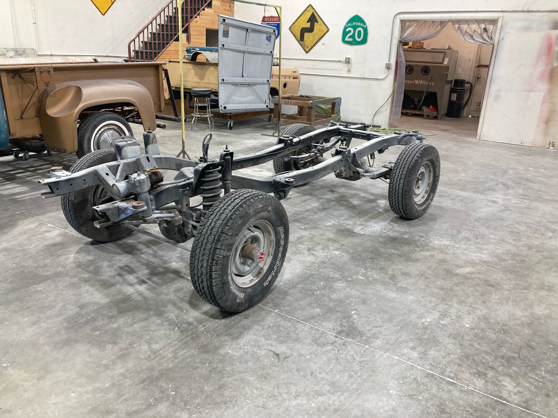 Car chassis frame with wheels in a garage, surrounded by workshop equipment and tools.