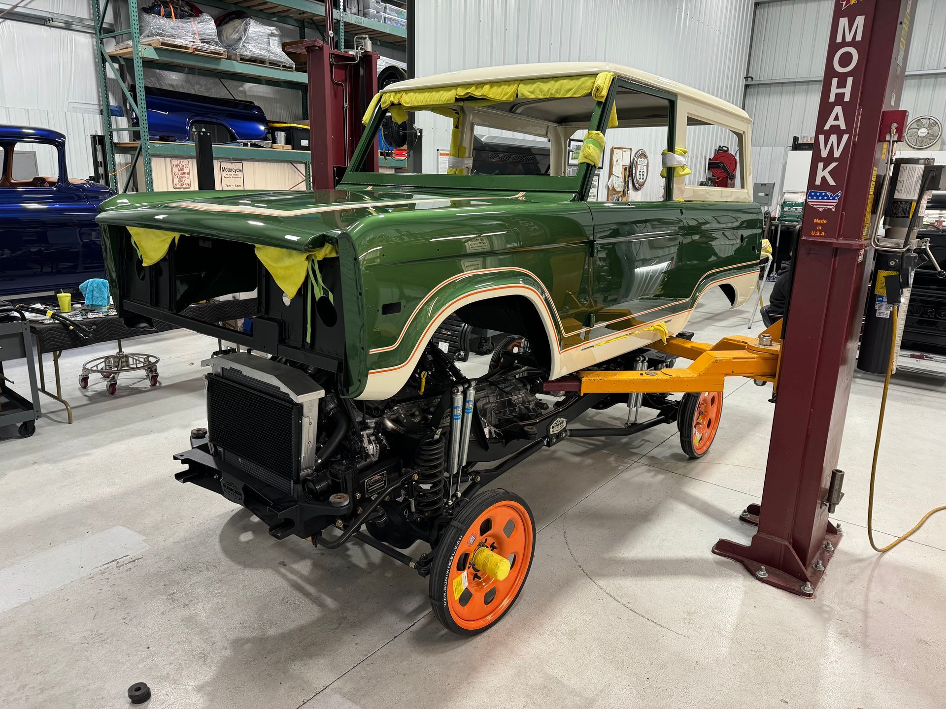 Green vintage SUV on a lift in an auto shop, with front end removed and a wheel attached.
