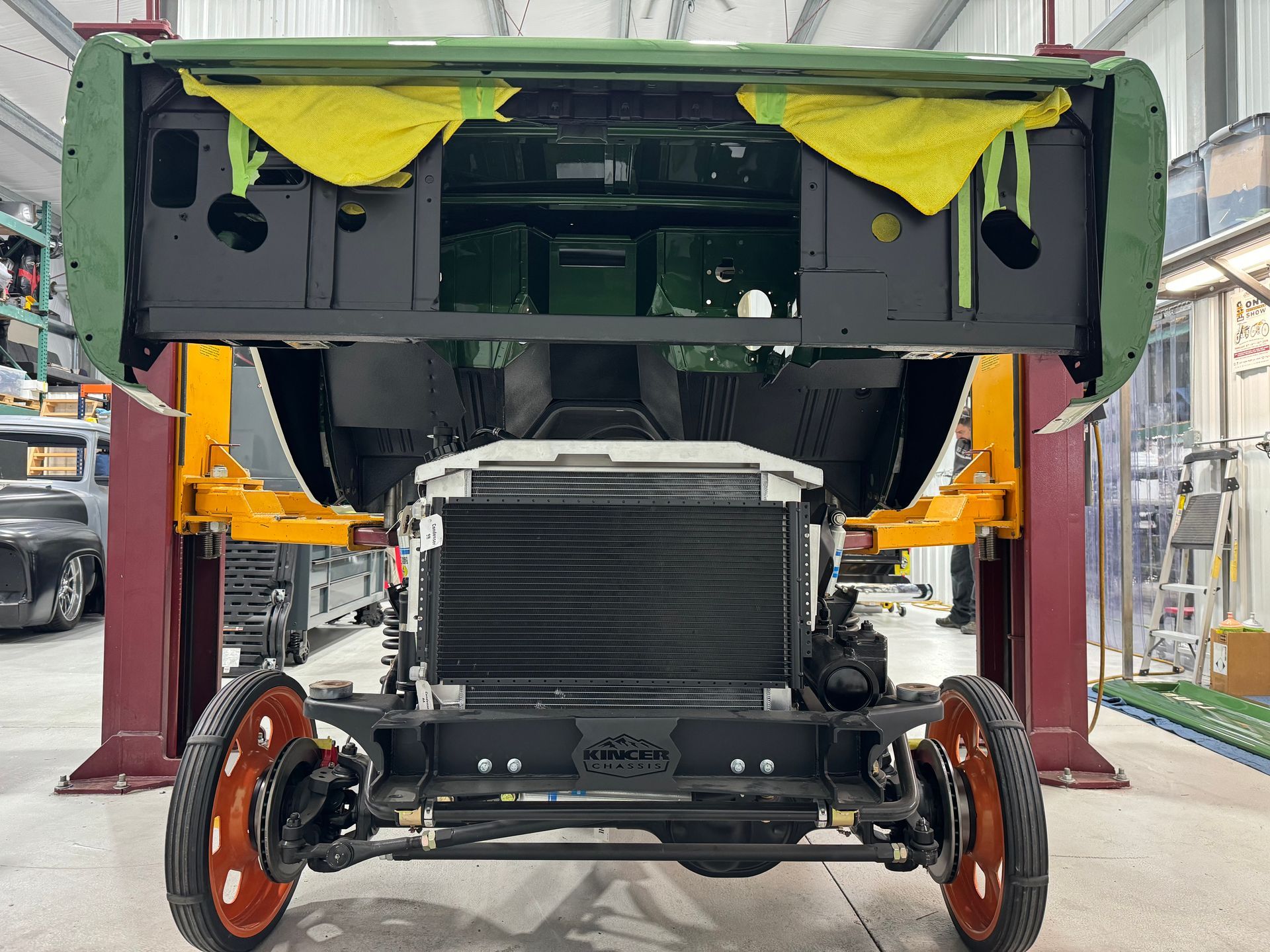 Vintage car chassis with exposed engine and red wheels in a workshop, front hood open.