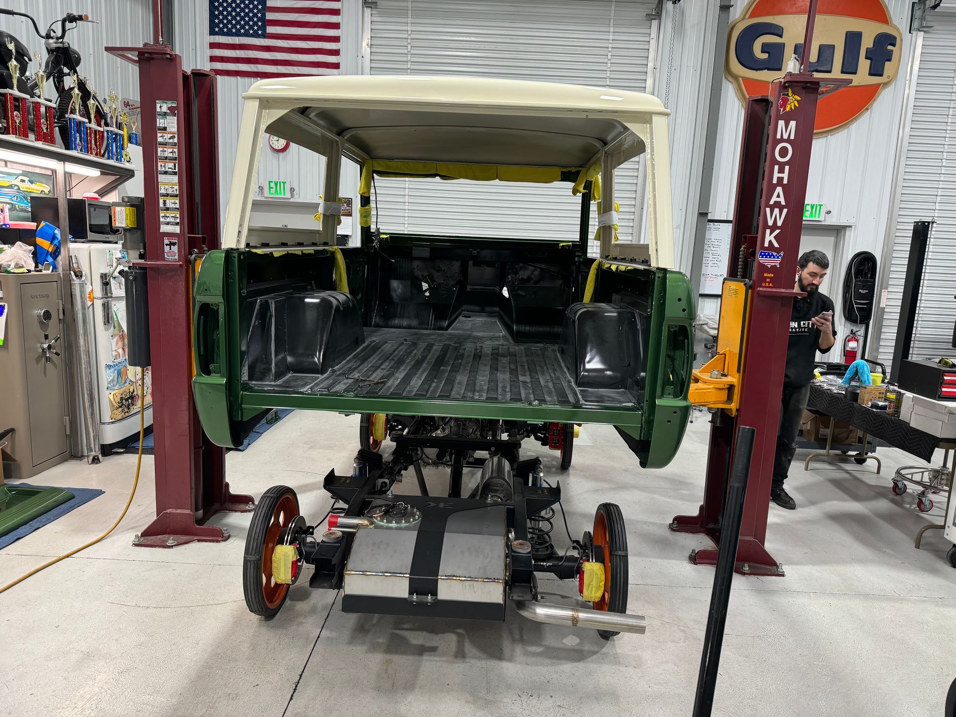 Vintage green Jeep on a lift in a garage, with its rear open and tools nearby.