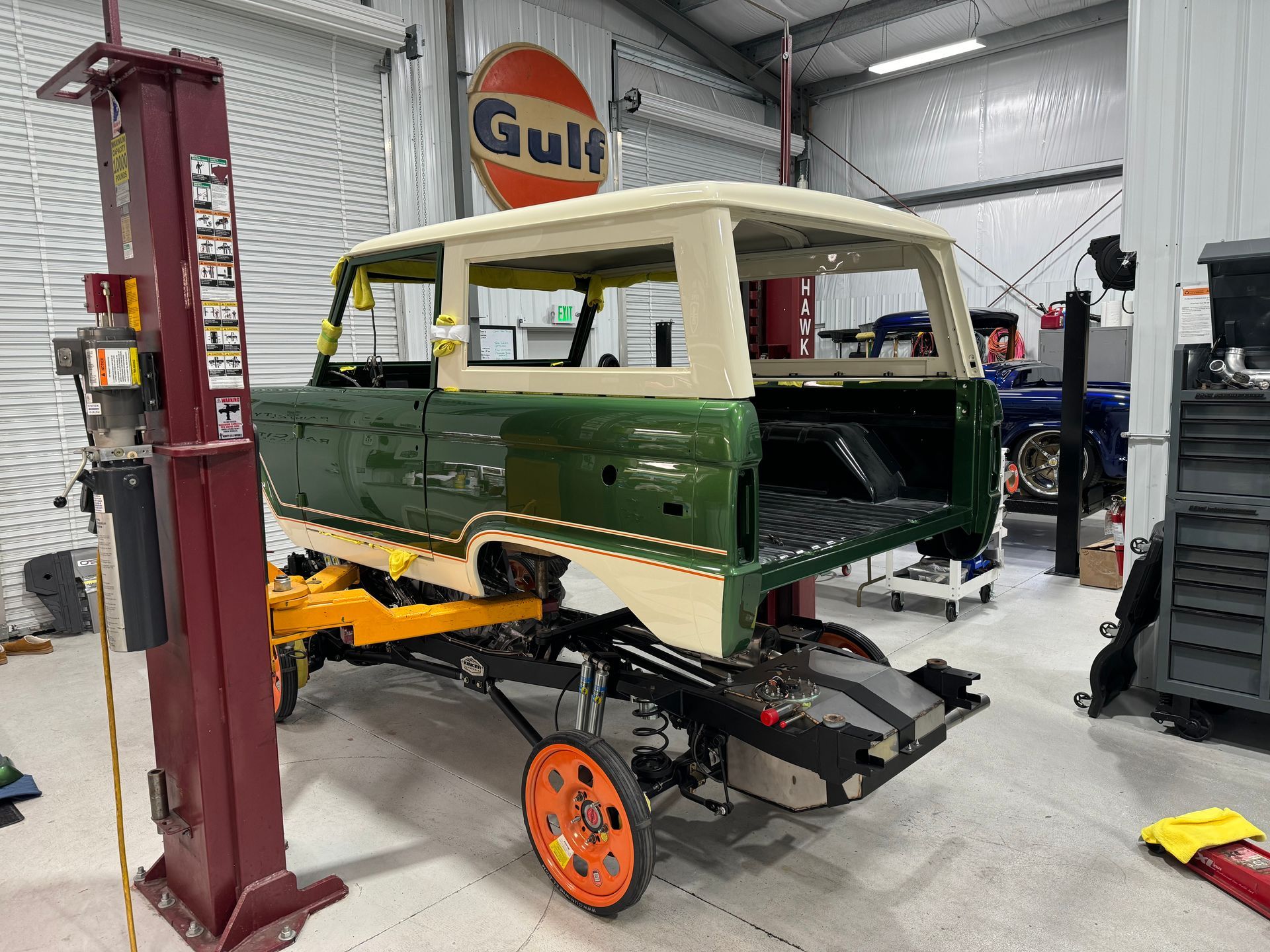 Partially restored green-and-cream vintage car body on a lift in an auto shop