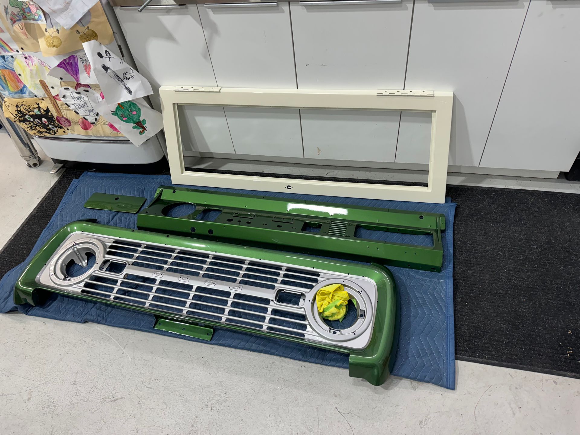 Disassembled green-and-white air conditioner parts on a blue mat in a room.