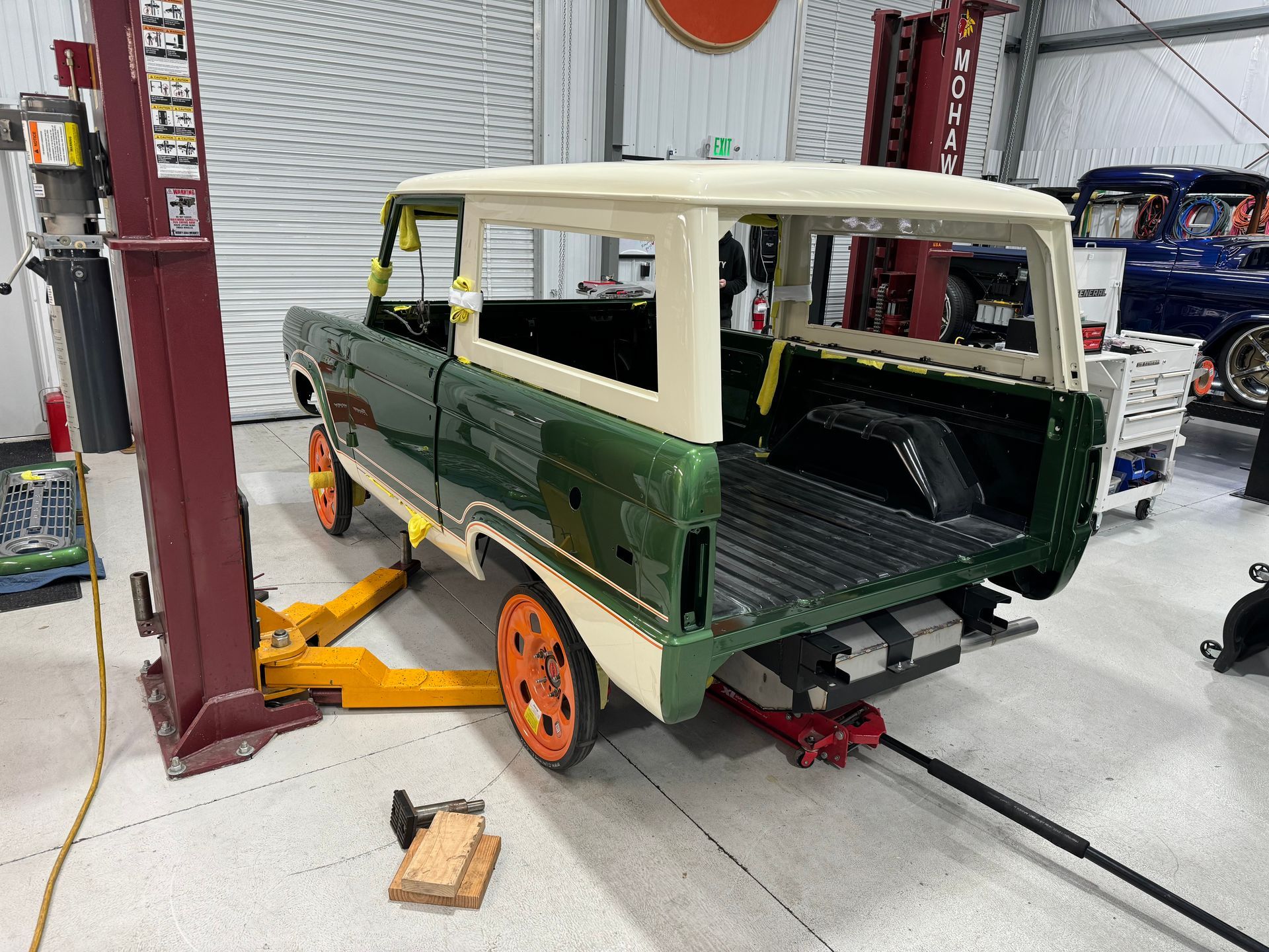 Partially restored vintage green SUV on a lift in an auto shop, with white roof and orange wheels