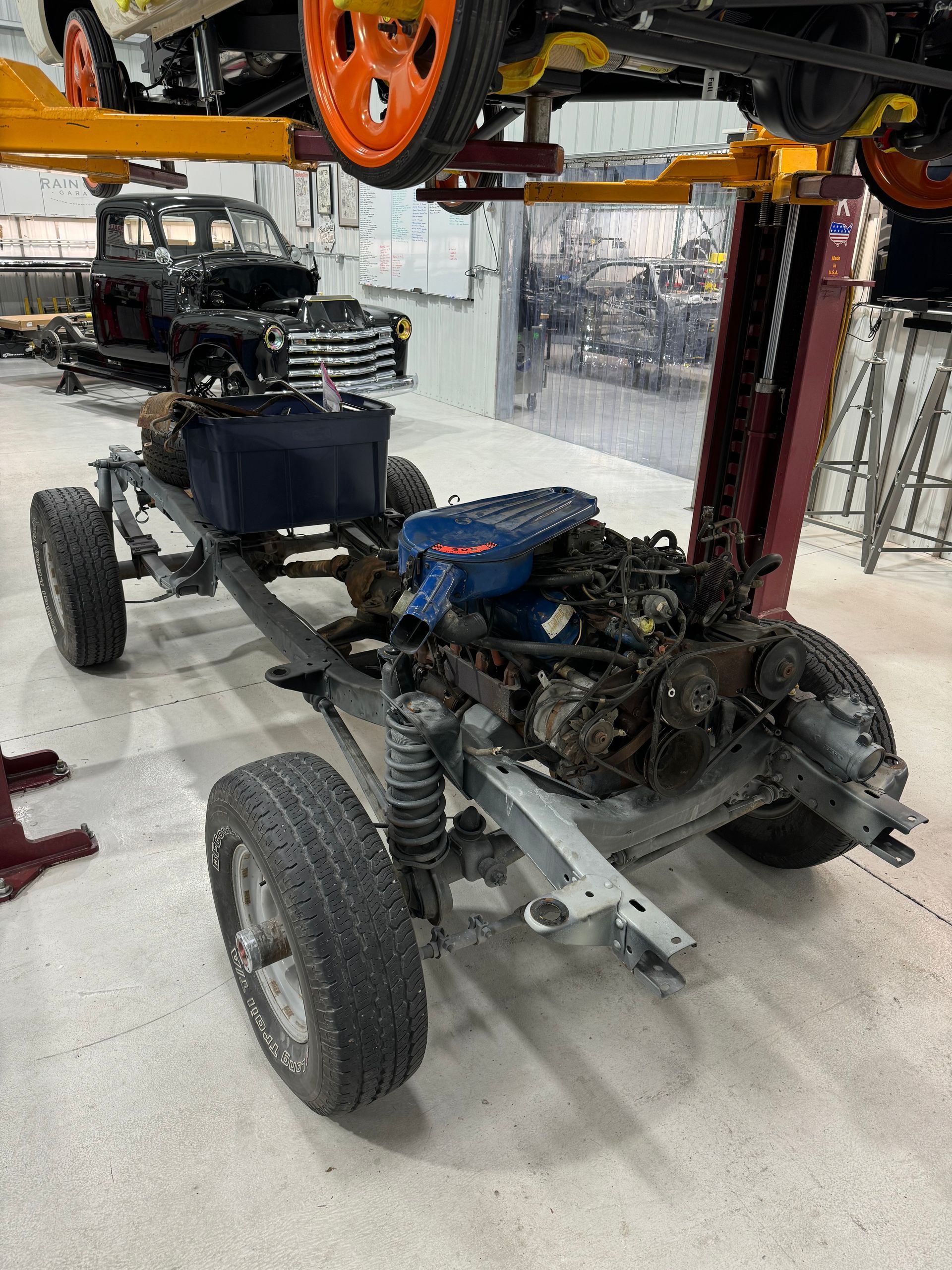Vehicle chassis on a lift in an auto shop, with exposed engine and suspension parts.