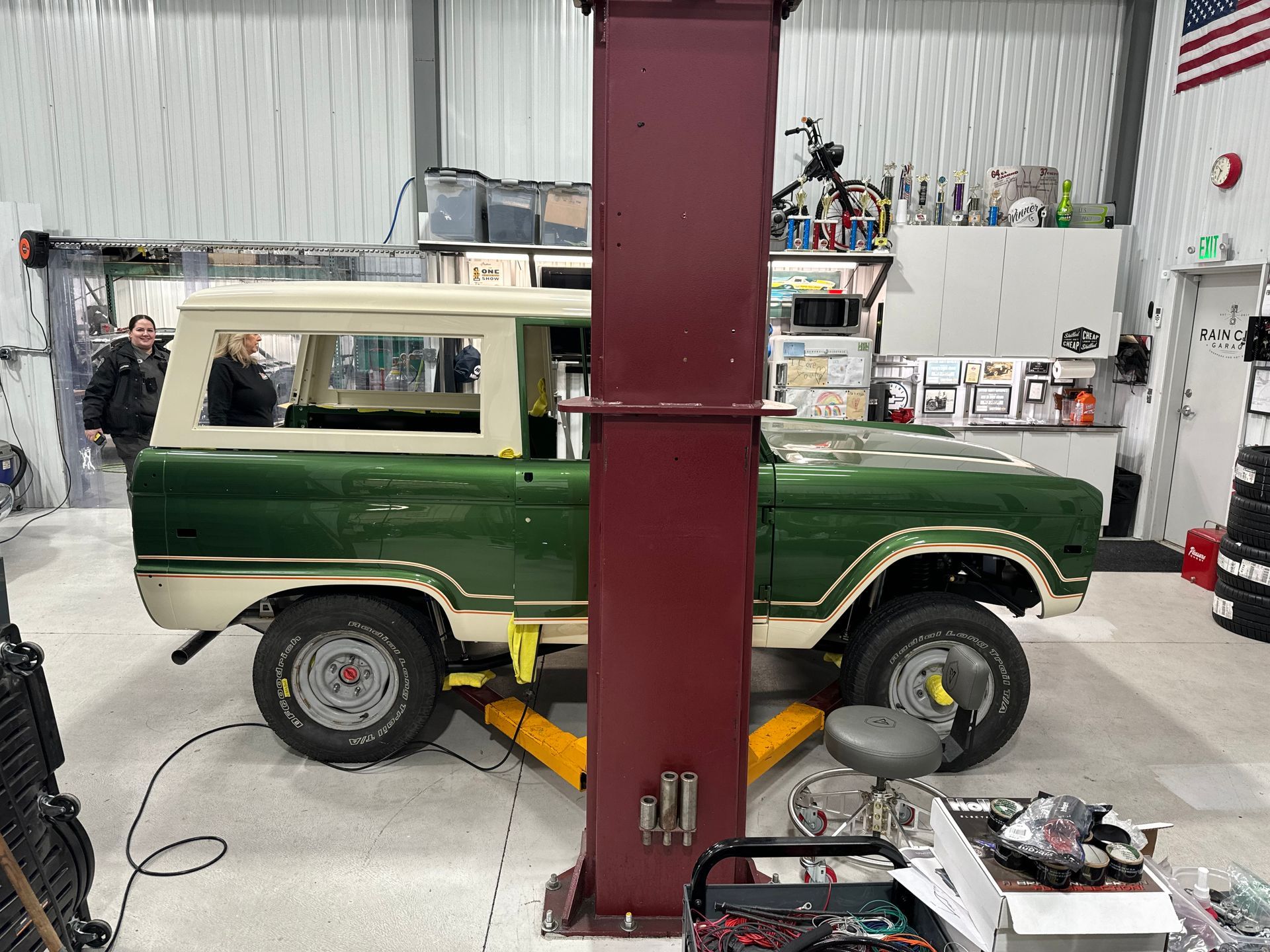 Green vintage SUV on a lift in a garage, with a cream hardtop and red support beam in front