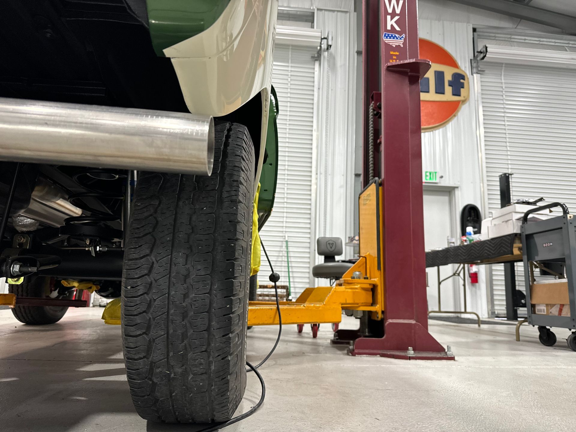 Car tire on a lift in an auto shop, with a red hydraulic post and equipment in the background