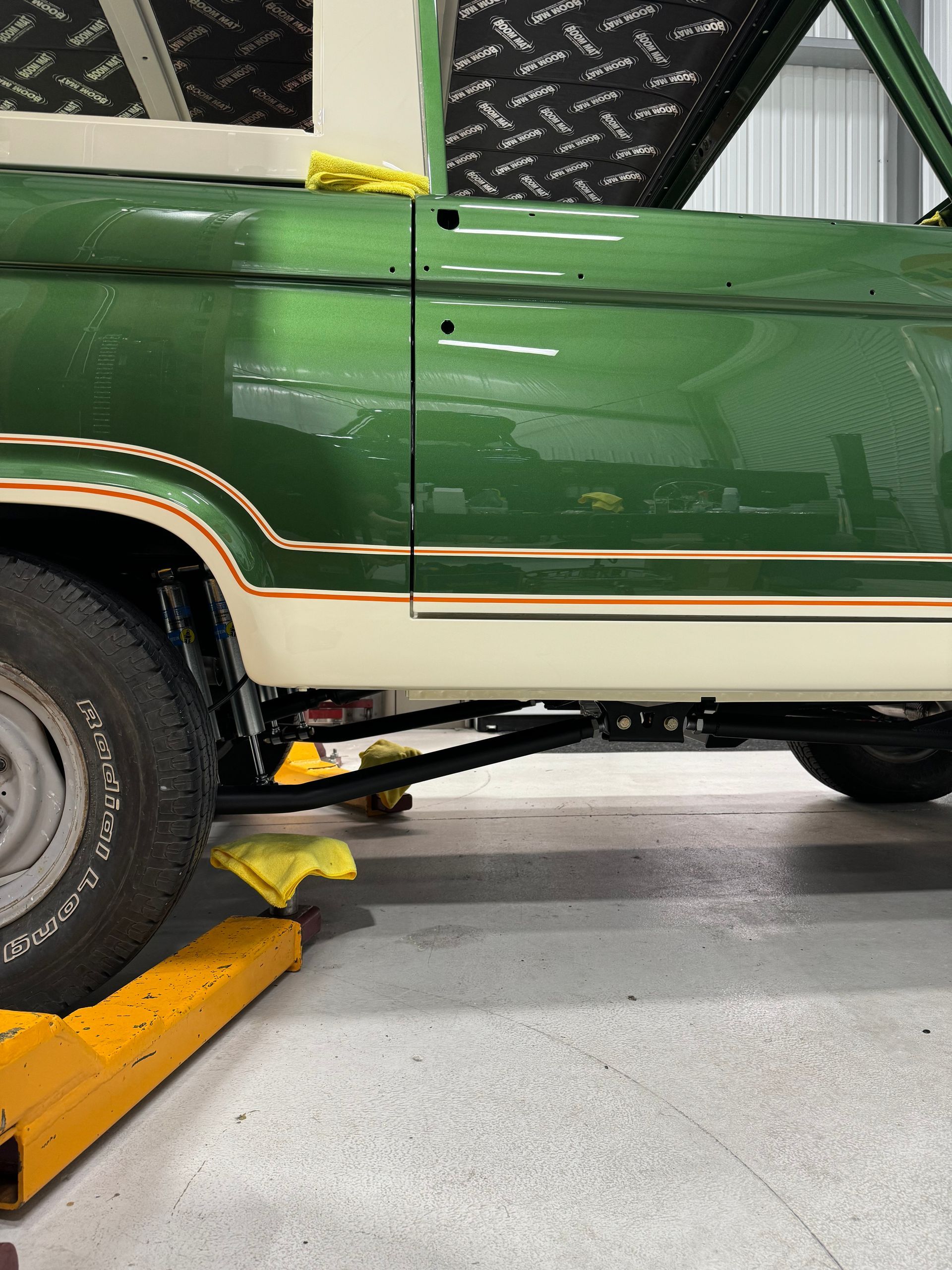 Green vintage truck partly lifted on a car jack in a garage, with yellow wheel chocks nearby