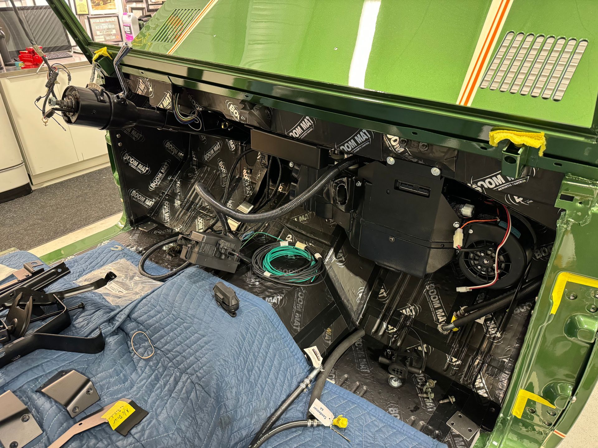 Partially disassembled green vehicle interior with exposed wiring and black components on a workshop floor
