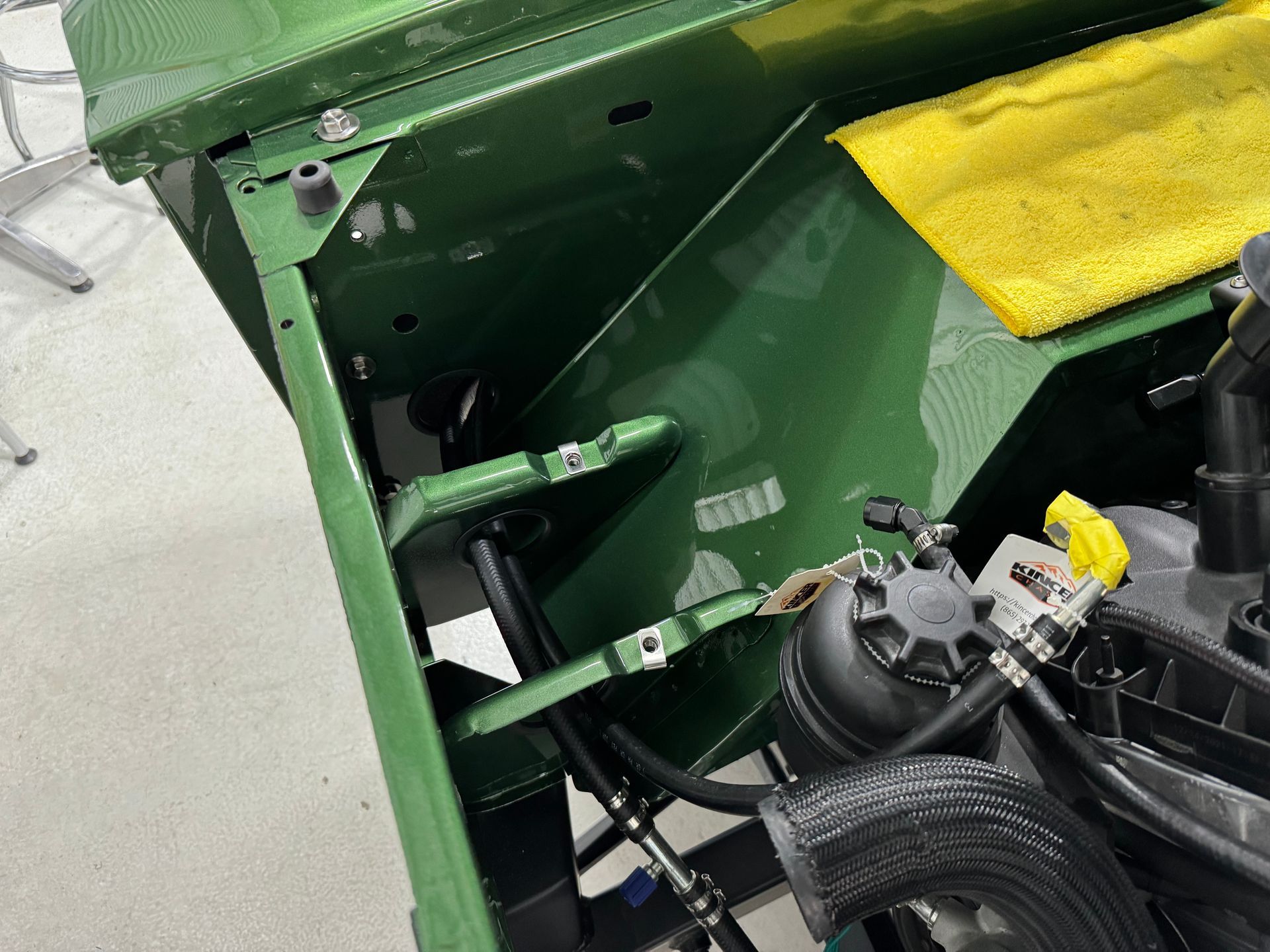 Green vehicle hood open, showing engine compartment with yellow cloth and visible steering components.