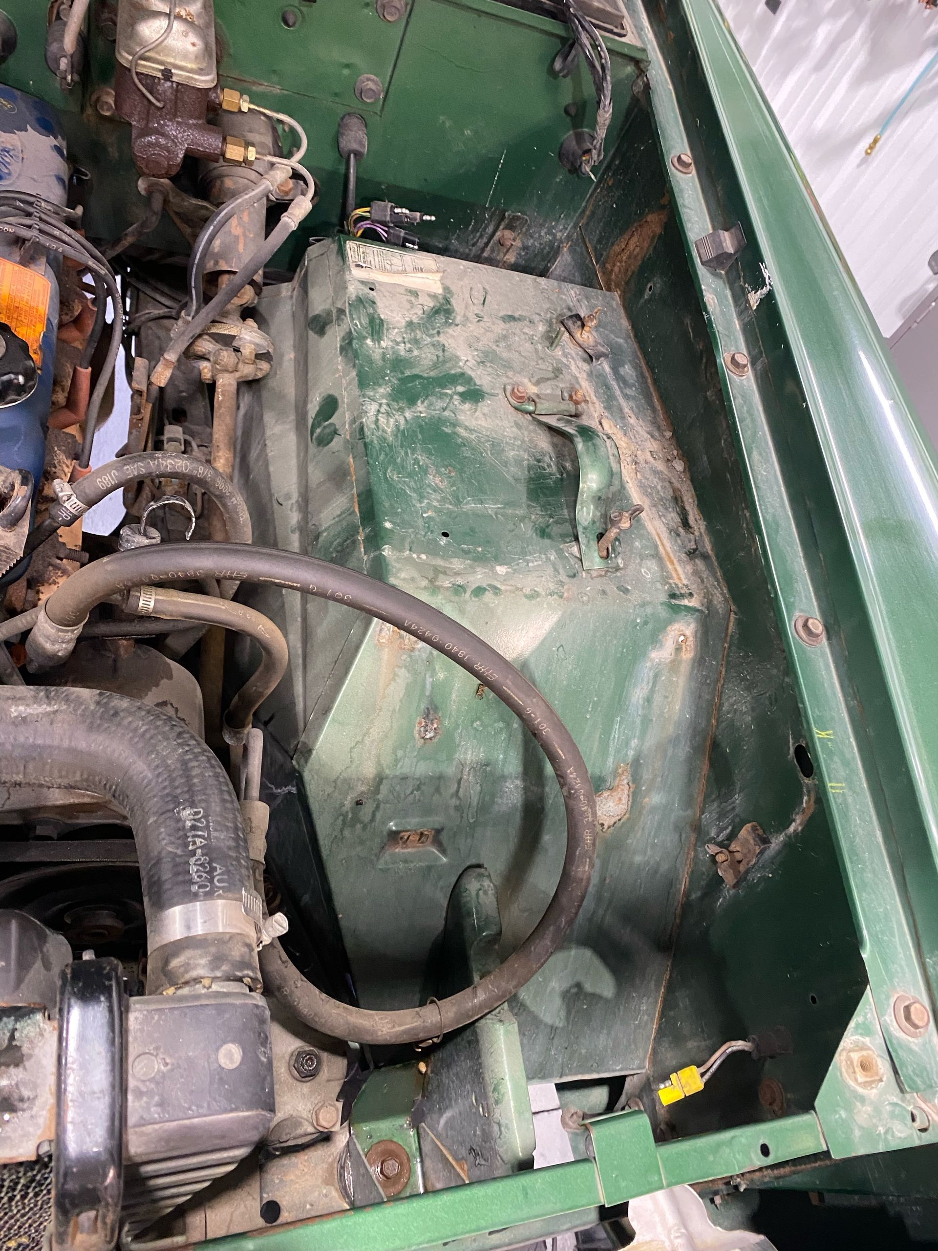 Close-up of a green vehicle engine bay with hoses, wiring, and mechanical parts exposed