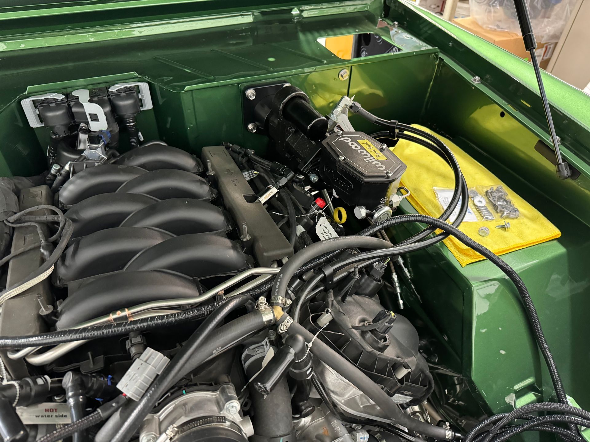 Green car engine bay with black intake manifold, hoses, and a yellow battery cover