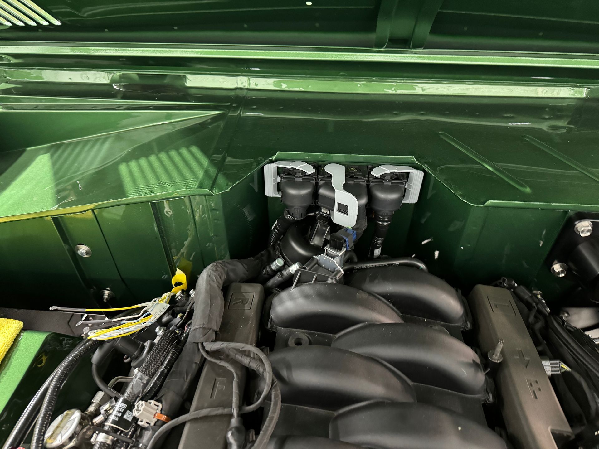 Green engine bay with a black intake manifold and visible hoses and components.