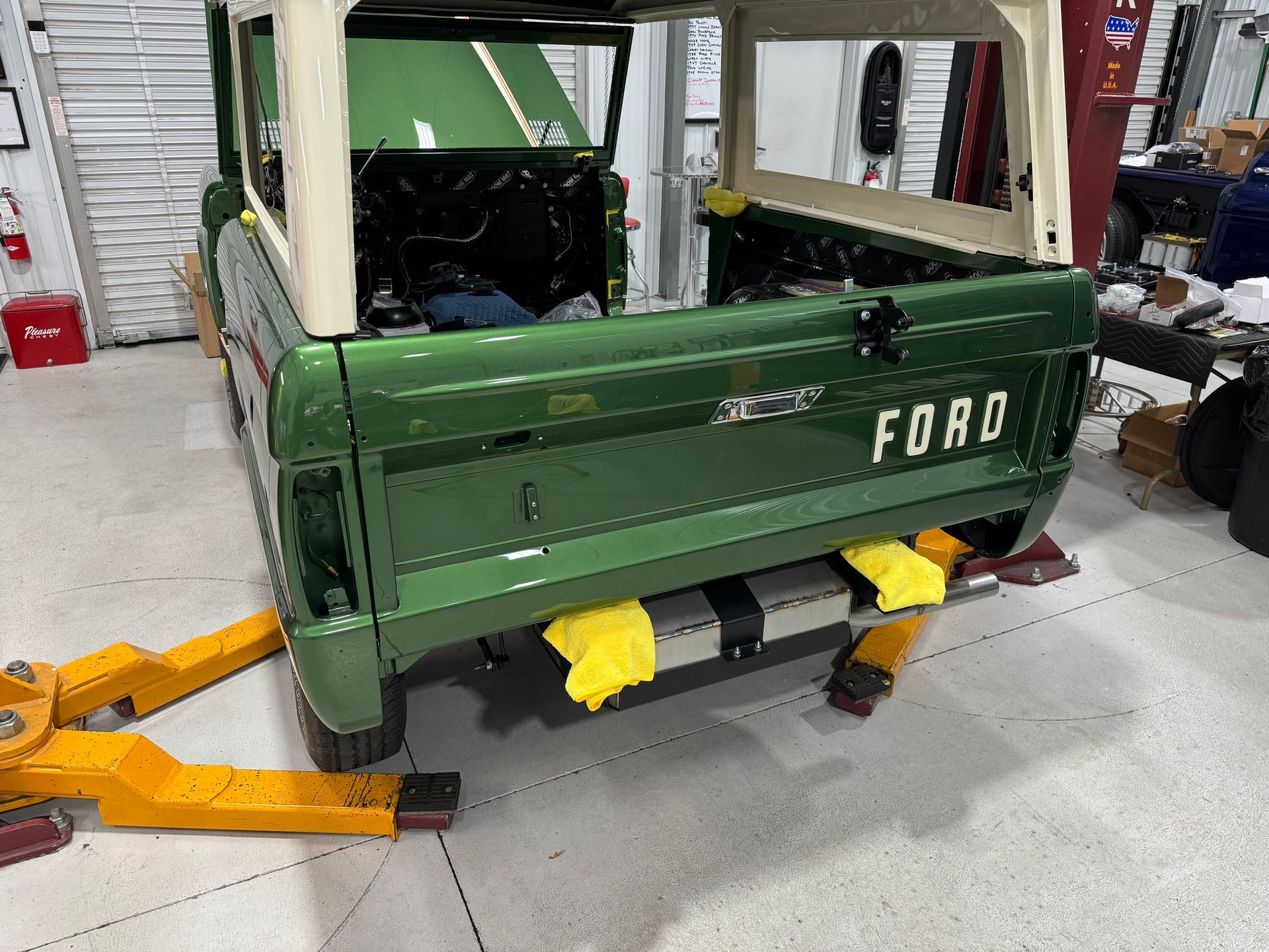 Green Ford pickup truck body in a workshop, raised on a yellow jack with the tailgate open.