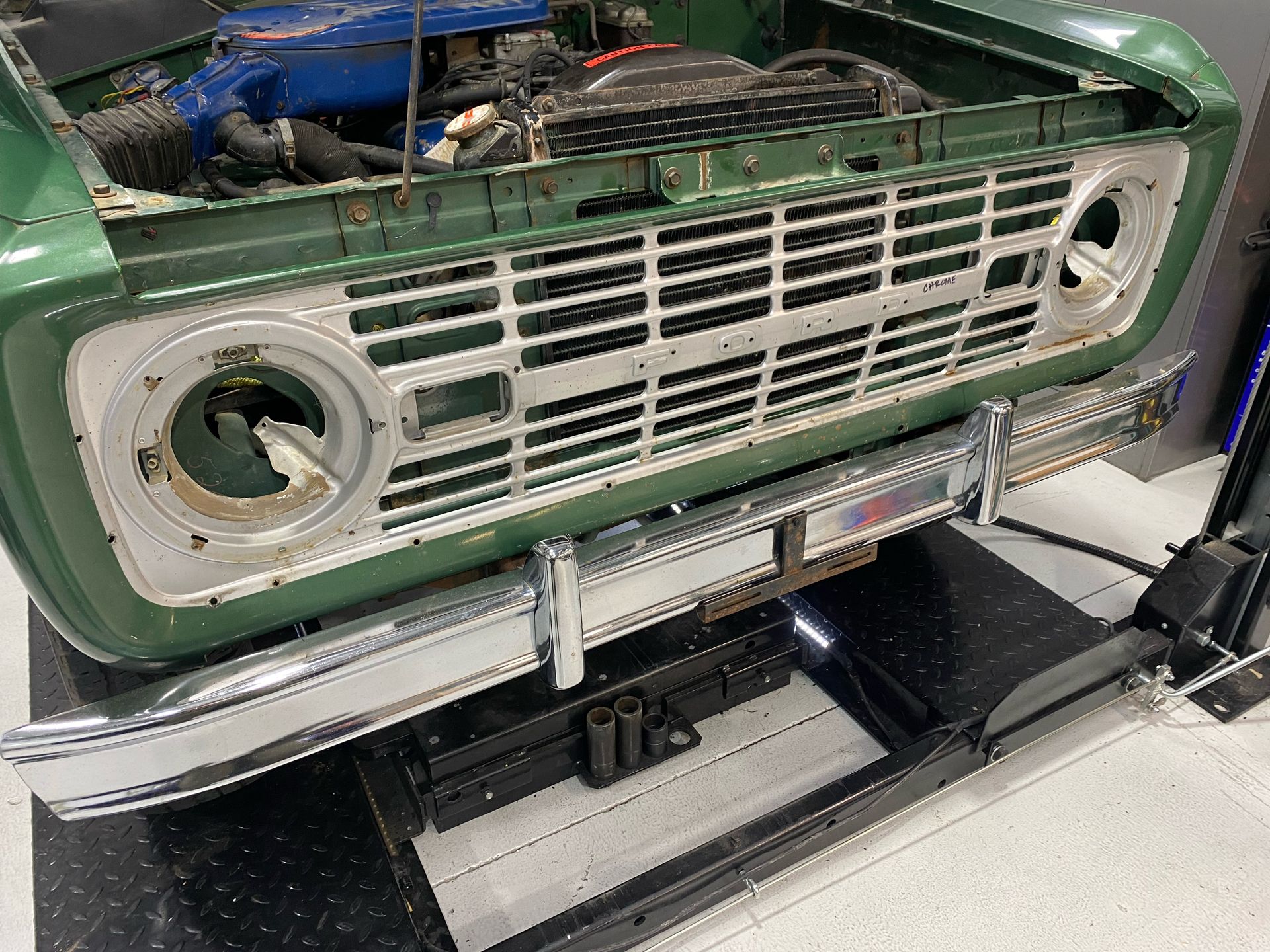 Front grille of a green vintage car mounted on a repair lift in a garage