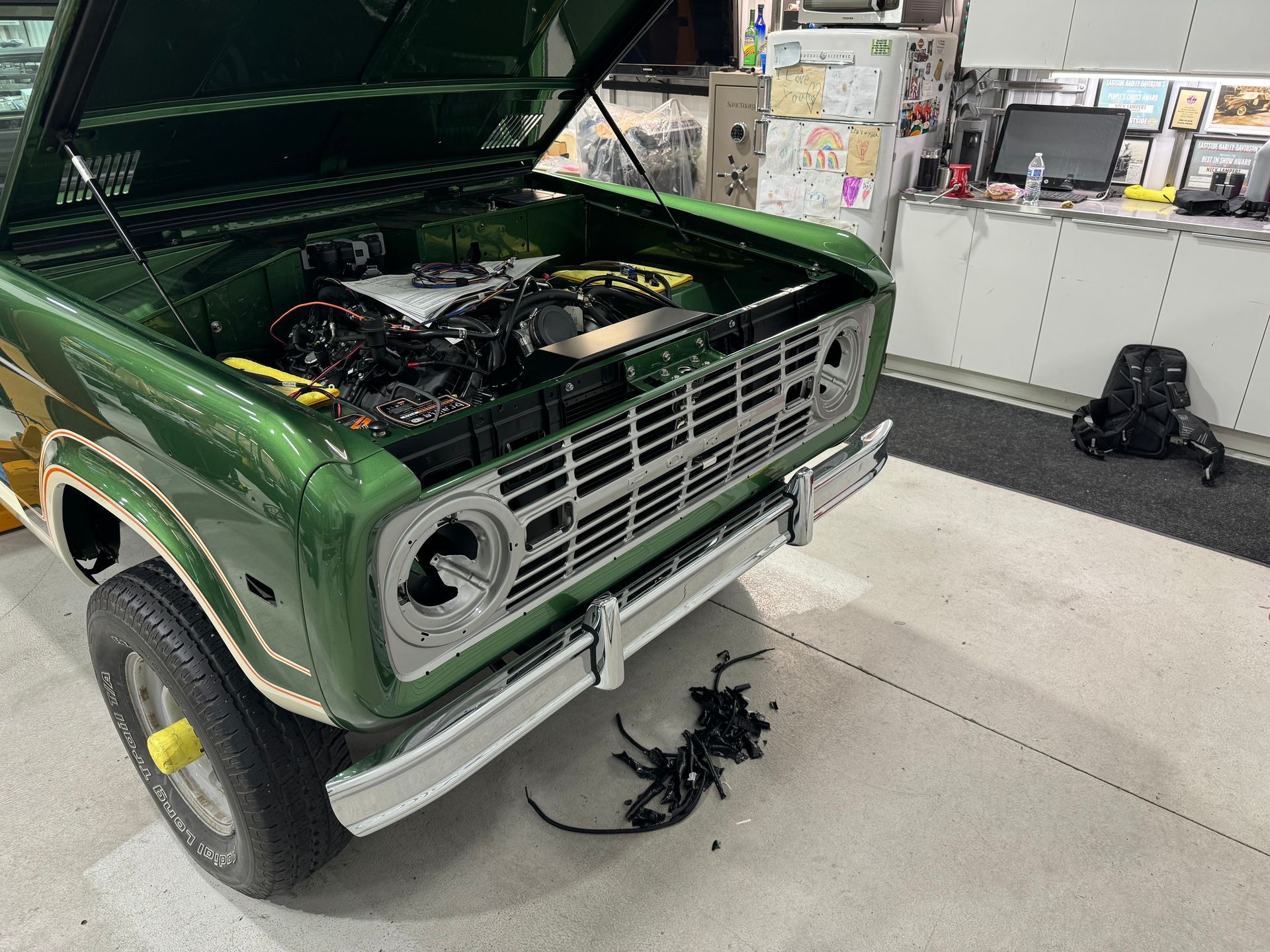Green off-road vehicle with open hood in a garage, engine exposed and a tool on the floor.