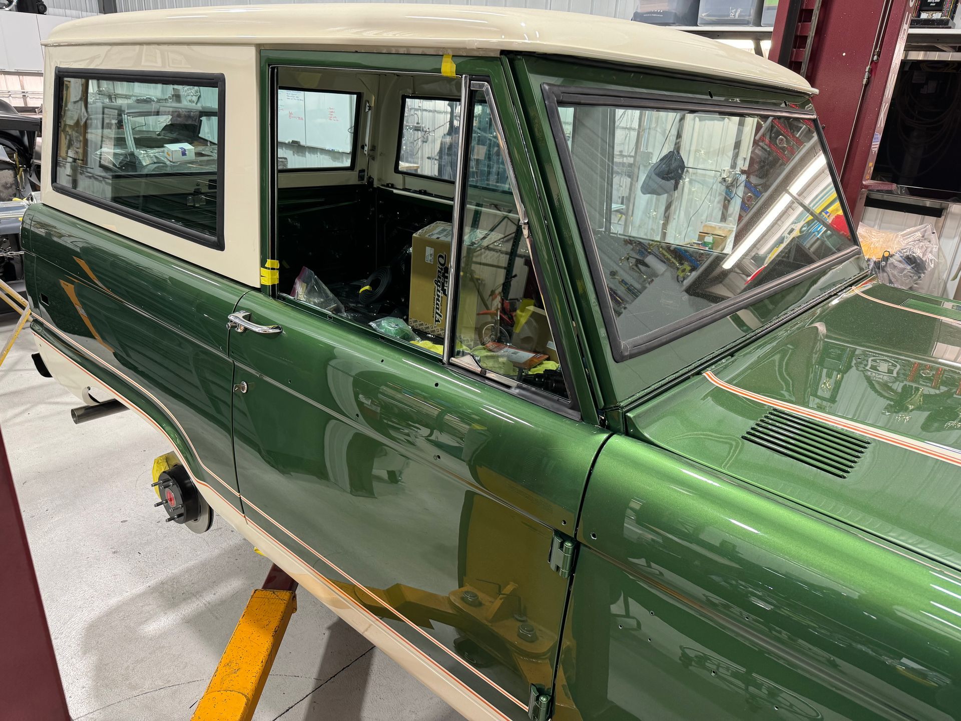 Green vintage car with cream roof in a garage, viewed from the side.