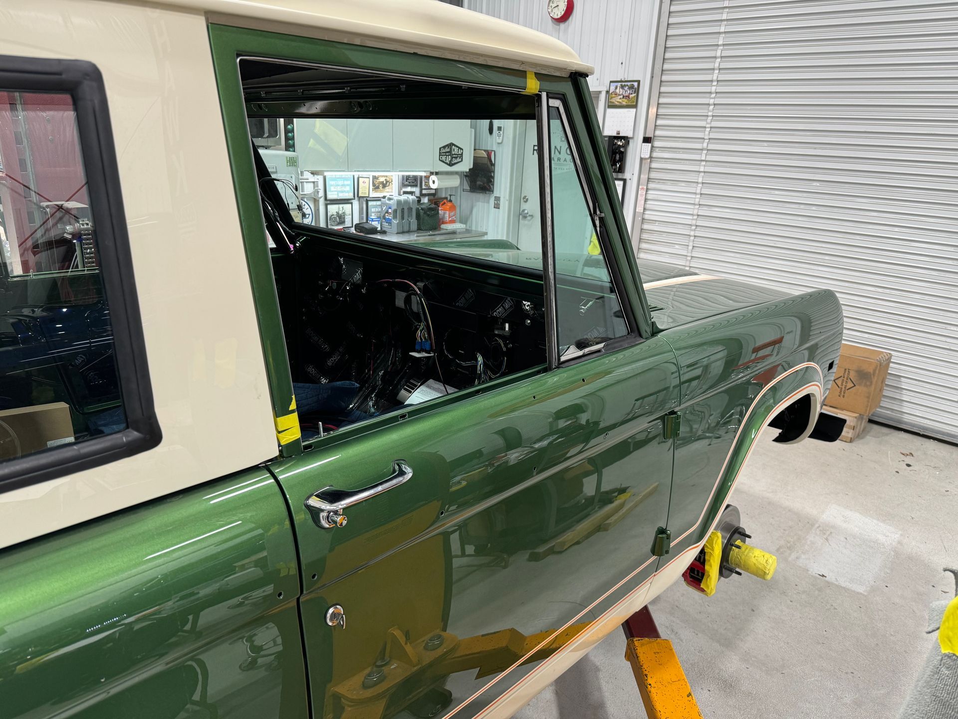 Green vintage SUV with tan roof in a garage, door open and front wheel removed for repair