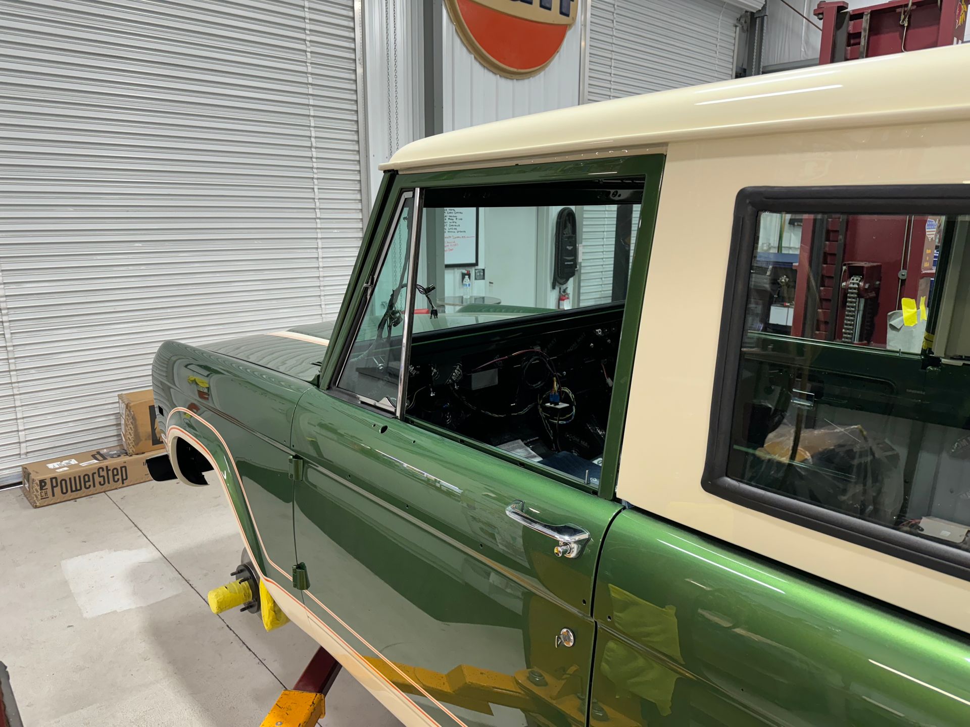 Green vintage SUV with beige roof in a workshop, raised on a jack with wheels removed
