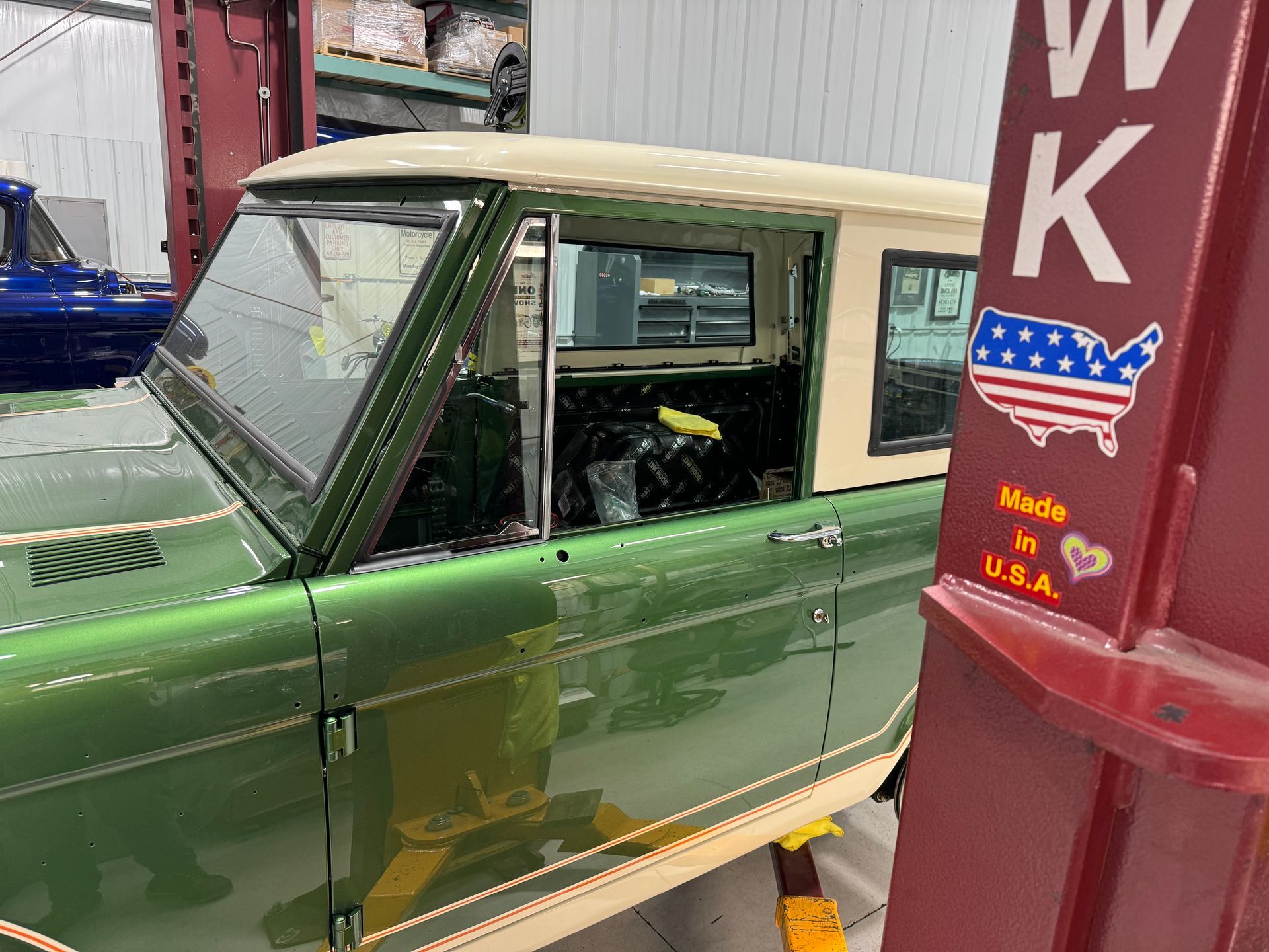 Green vintage car in a garage, with a beige roof and red equipment beside it.