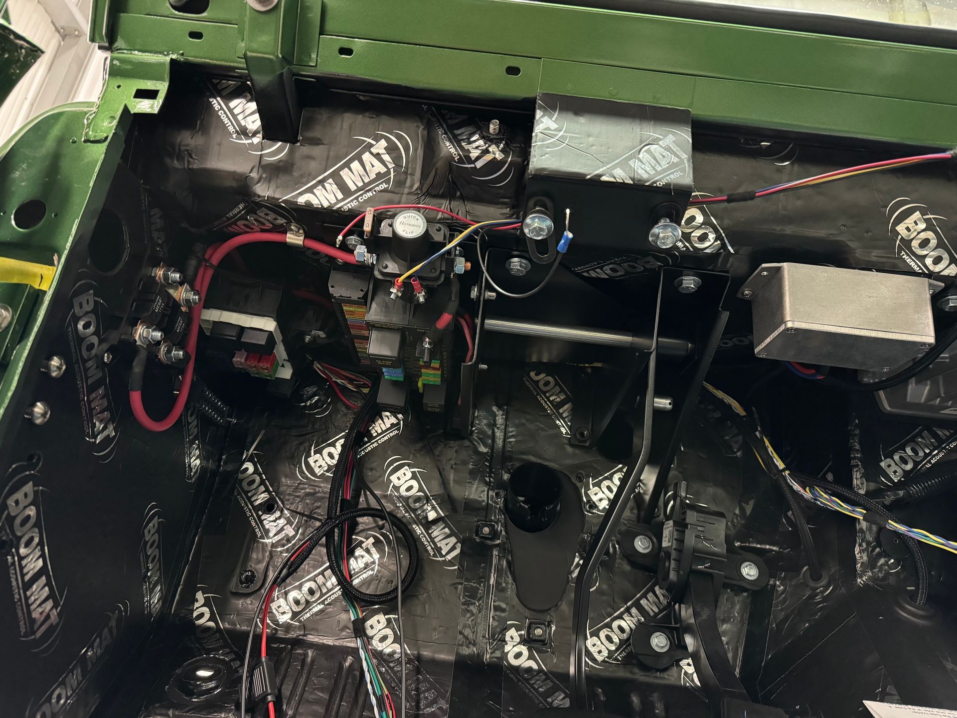 Close-up of a wet, cluttered engine compartment with black components, red wiring, and green body panels.
