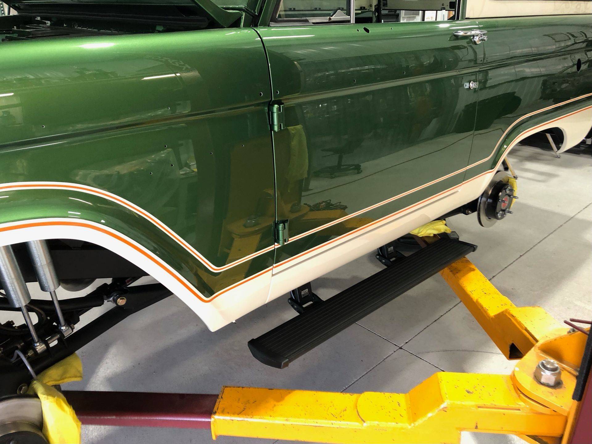 Classic dark green car lifted on a yellow hydraulic jack in a garage.