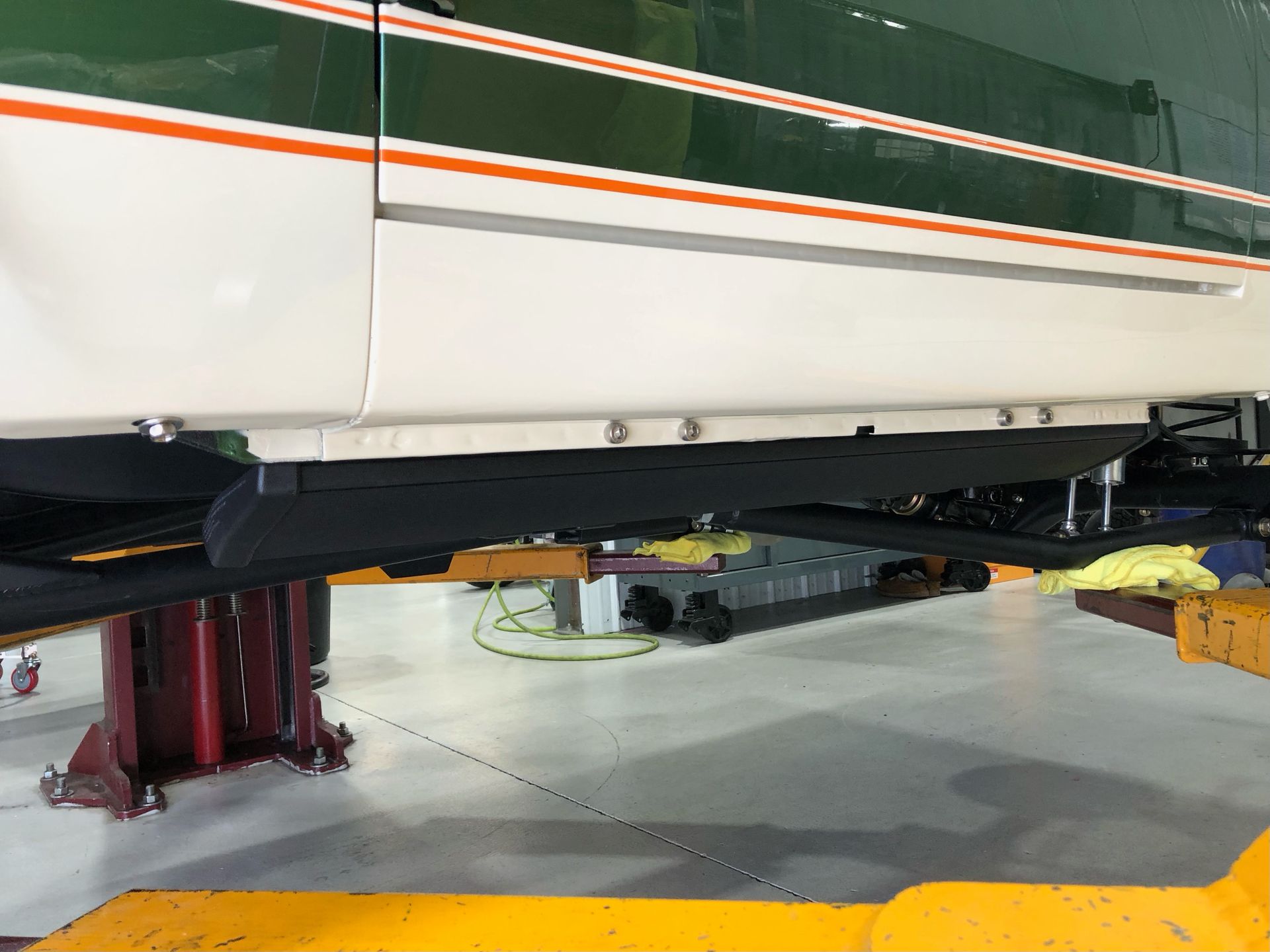White vehicle lifted on garage jacks, with orange stripe along the side in a workshop.
