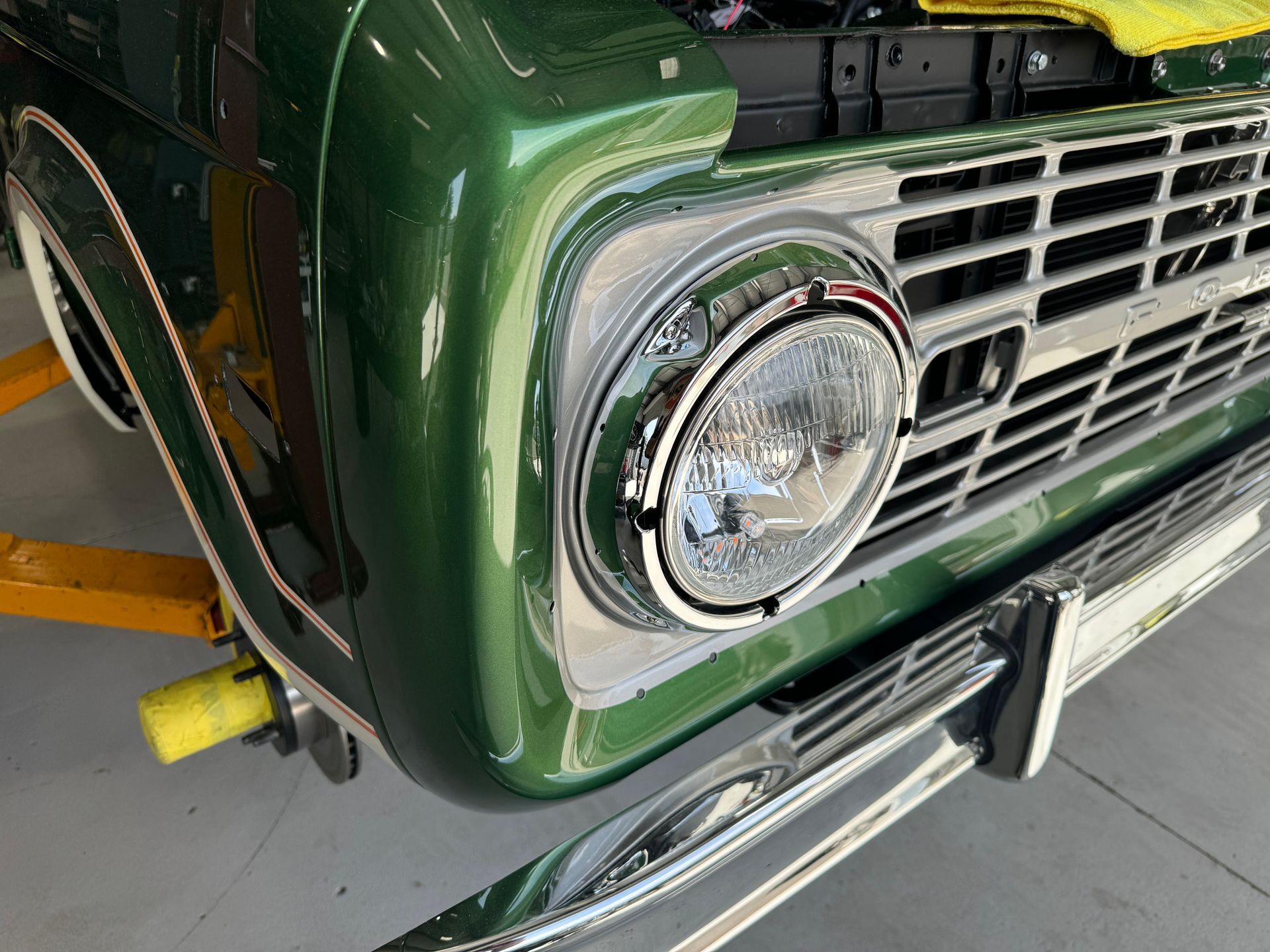 Close-up of a green vintage truck front with chrome grille and round headlight in a garage