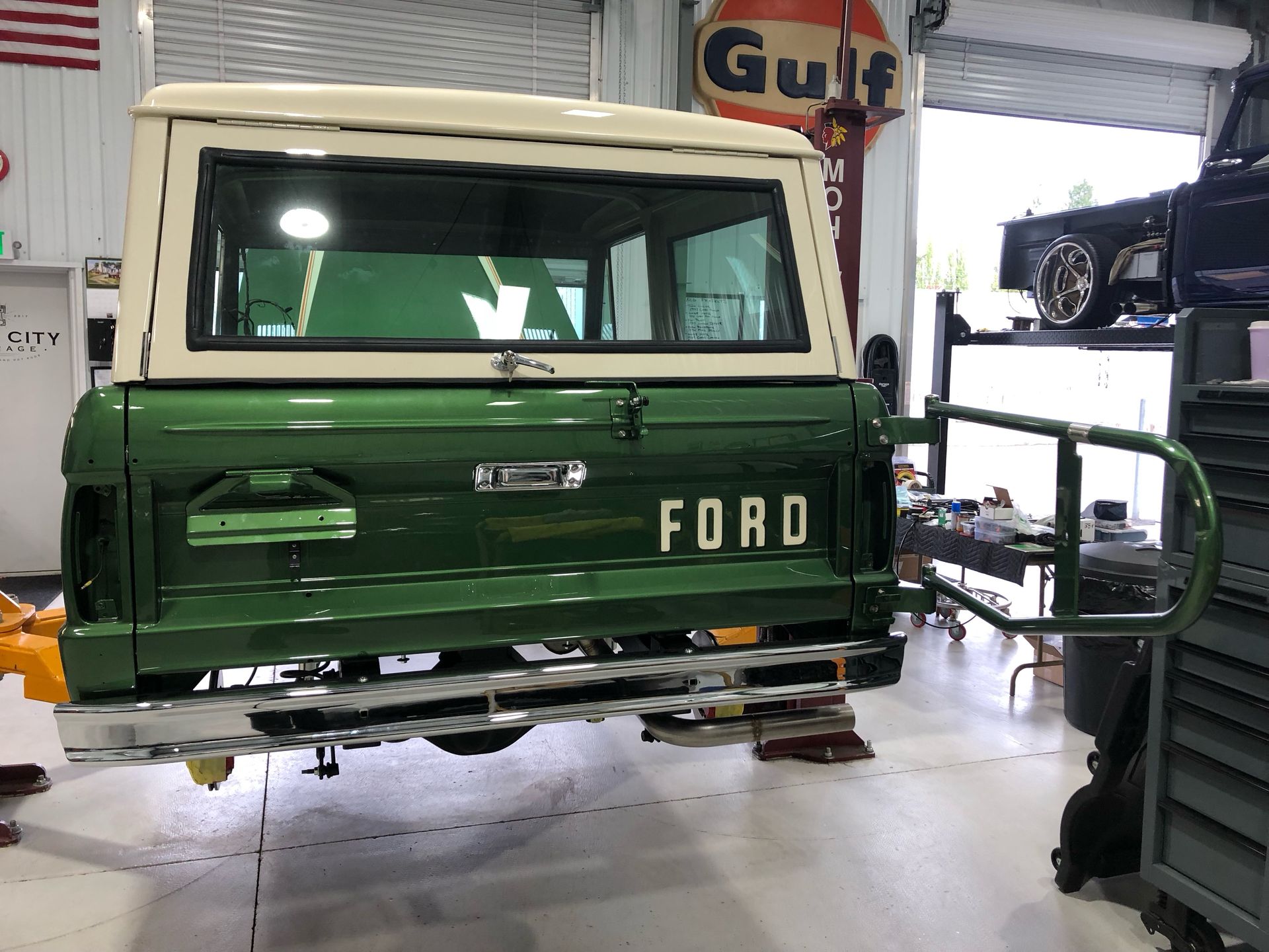 Rear view of a green Ford truck in a garage, with a white cab and workshop equipment nearby