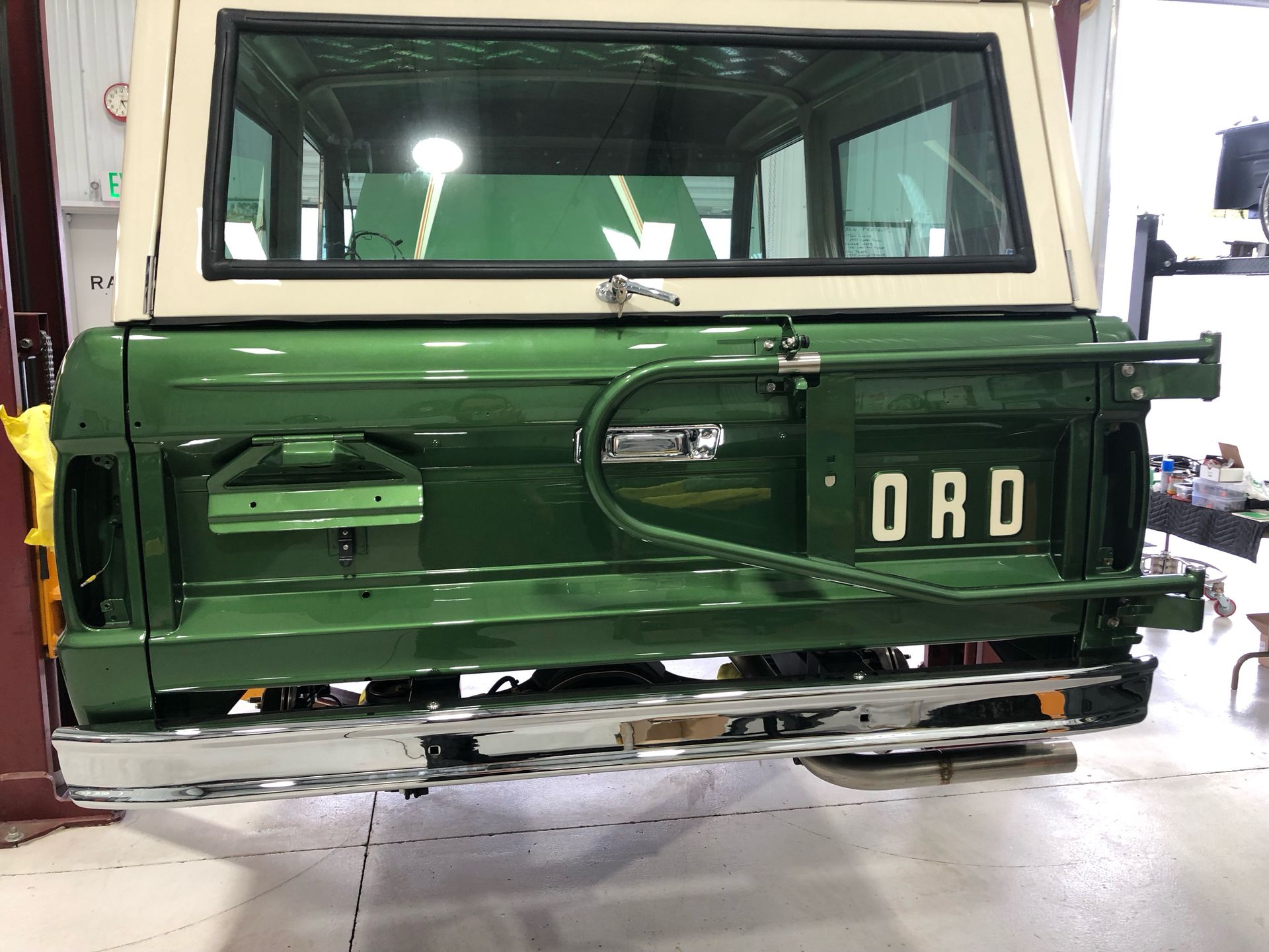 Green vintage truck with white cab, rear tailgate open in a garage or workshop