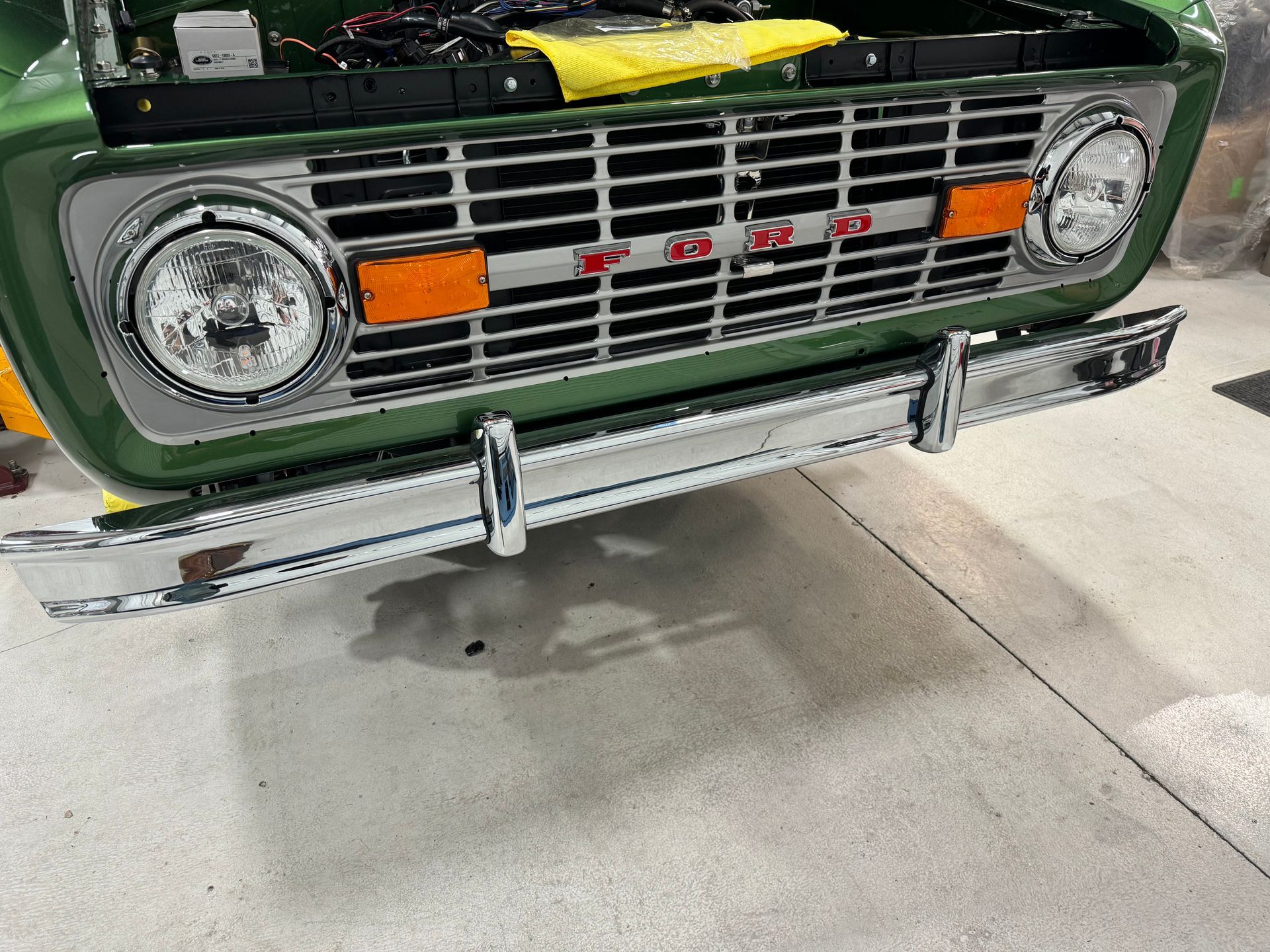 Front view of a green vintage Ford Bronco with chrome grille and bumper on a concrete floor