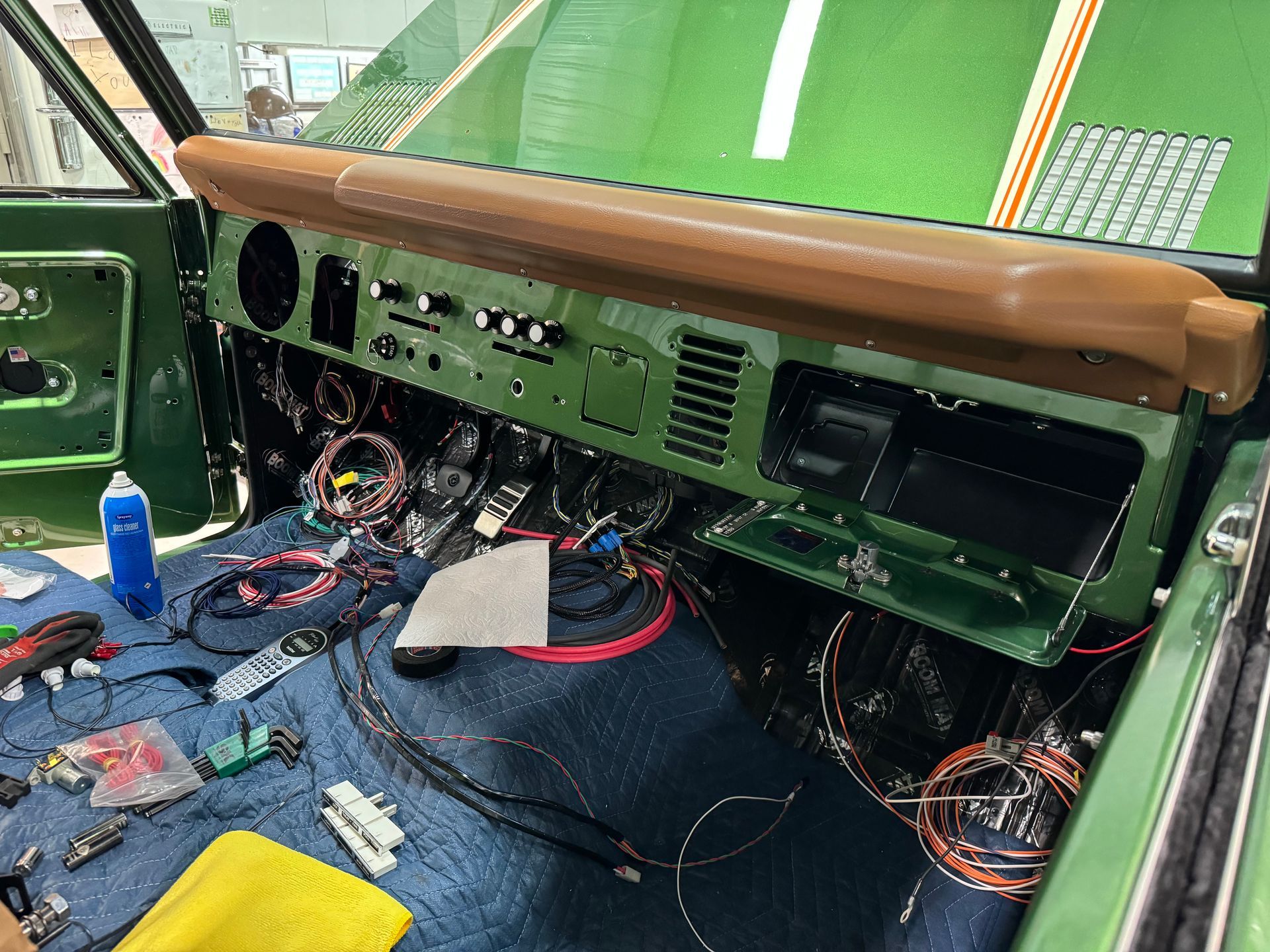 Damaged car interior with exposed wiring, torn blue floor covering, and a green dashboard under a brown padded rail