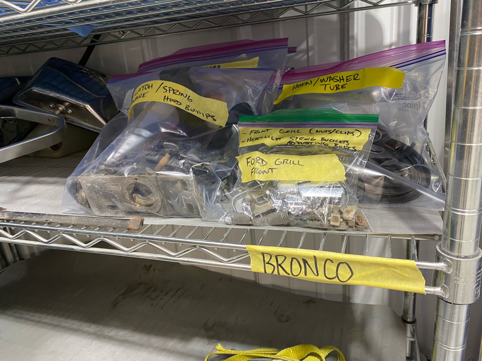 Metal shelf with labeled plastic bags of parts and a yellow tape tag reading “BRONCO”