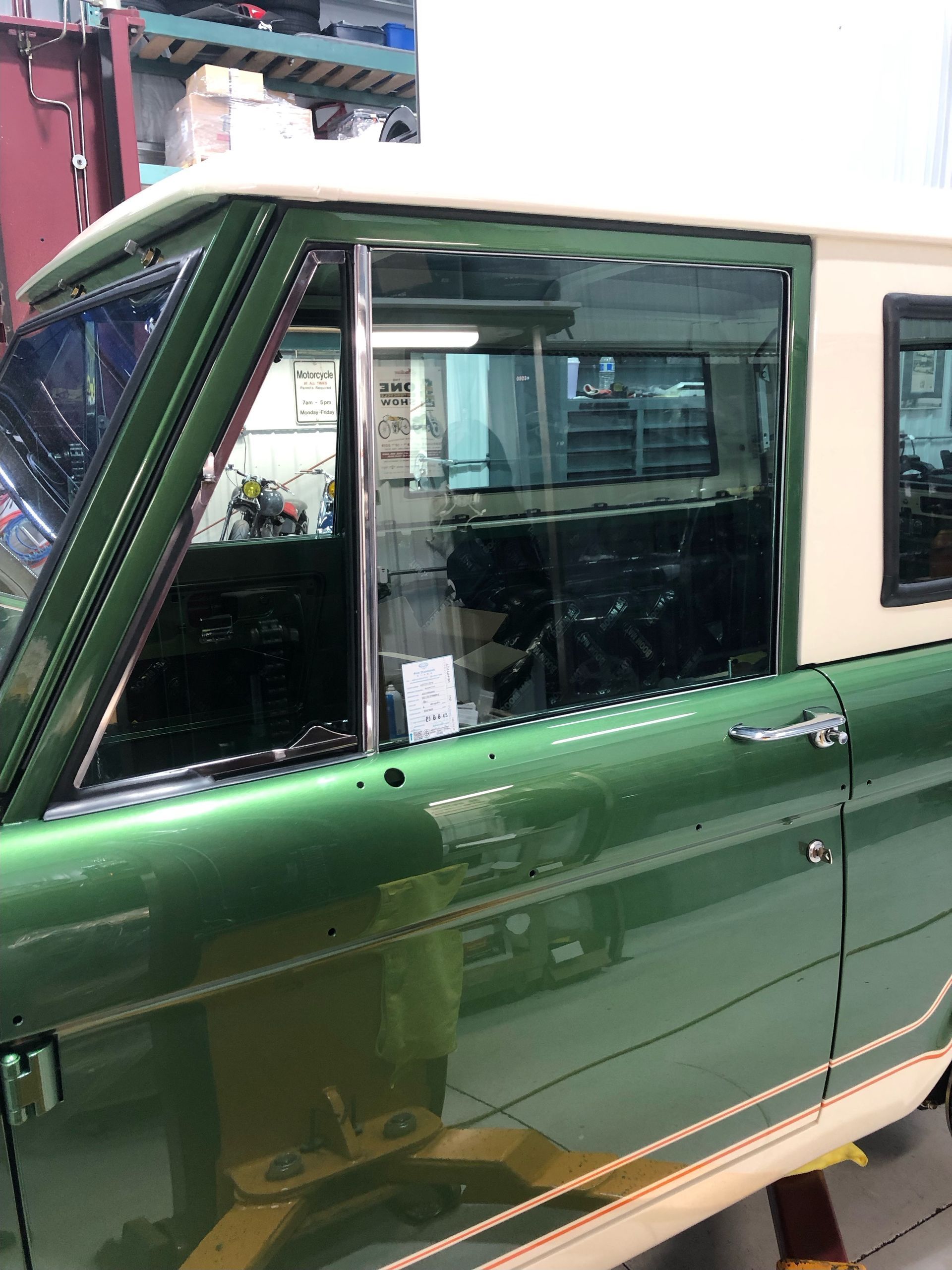 Green vintage car door and side window inside a garage, with a chrome mirror and trim.