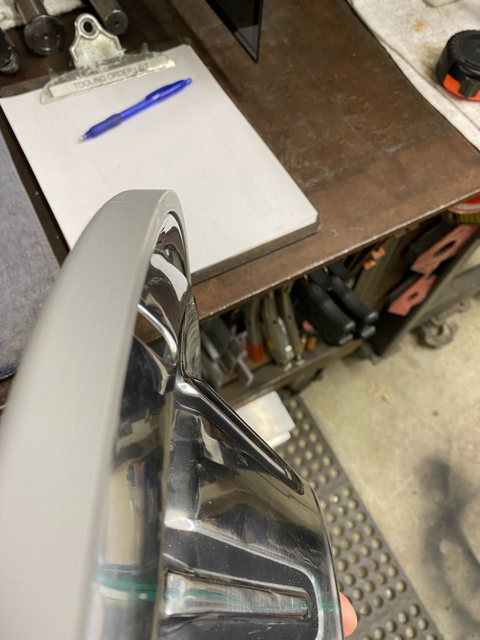 Close-up of a car headlight assembly on a workbench next to a clipboard and pen