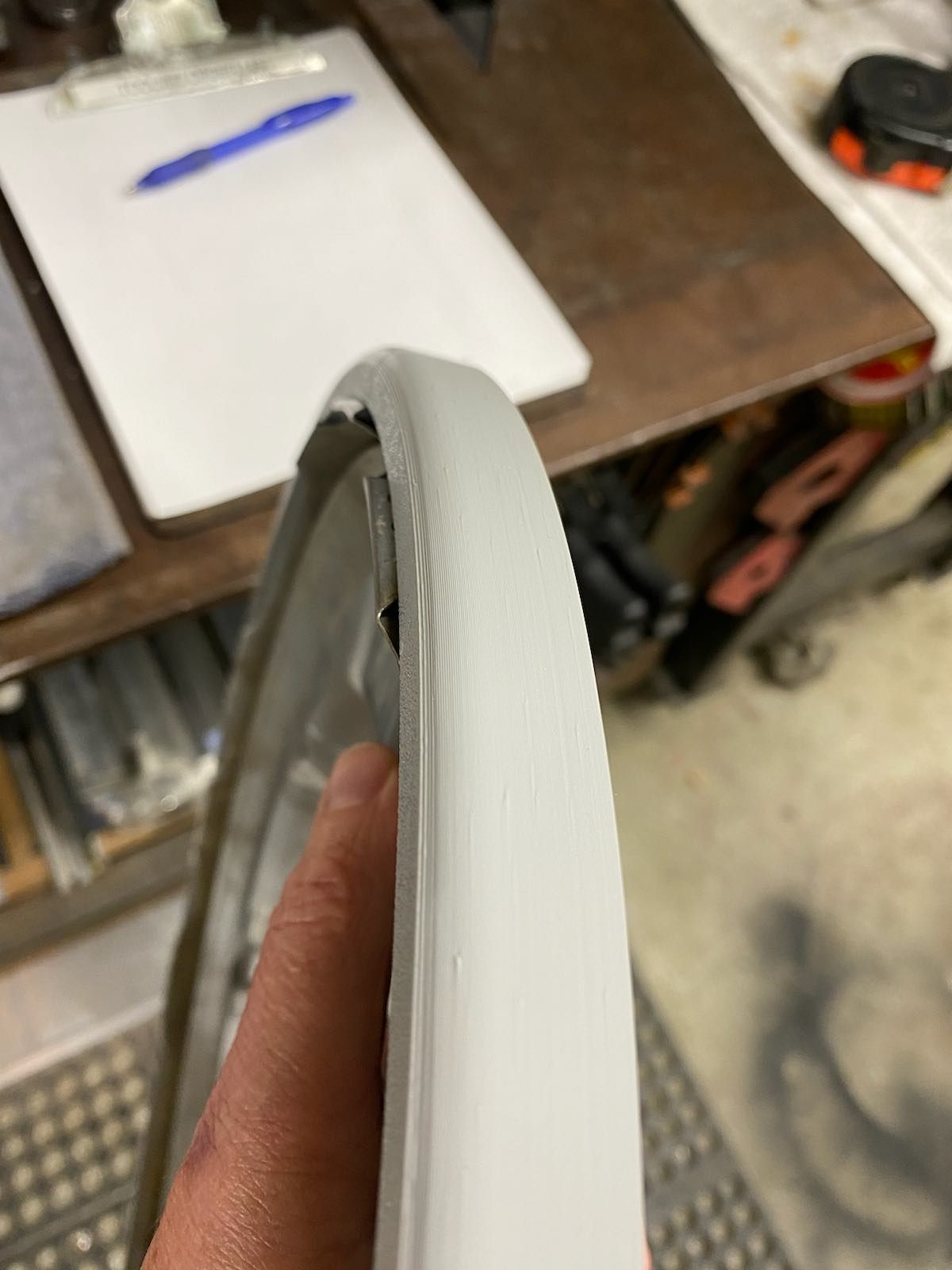 Close-up of a white wheel rim being held by a hand in a workshop.