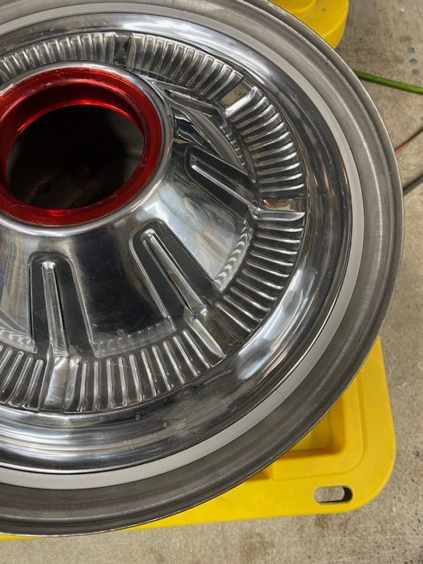 Close-up of a shiny metal car wheel rim with a red center on a yellow surface