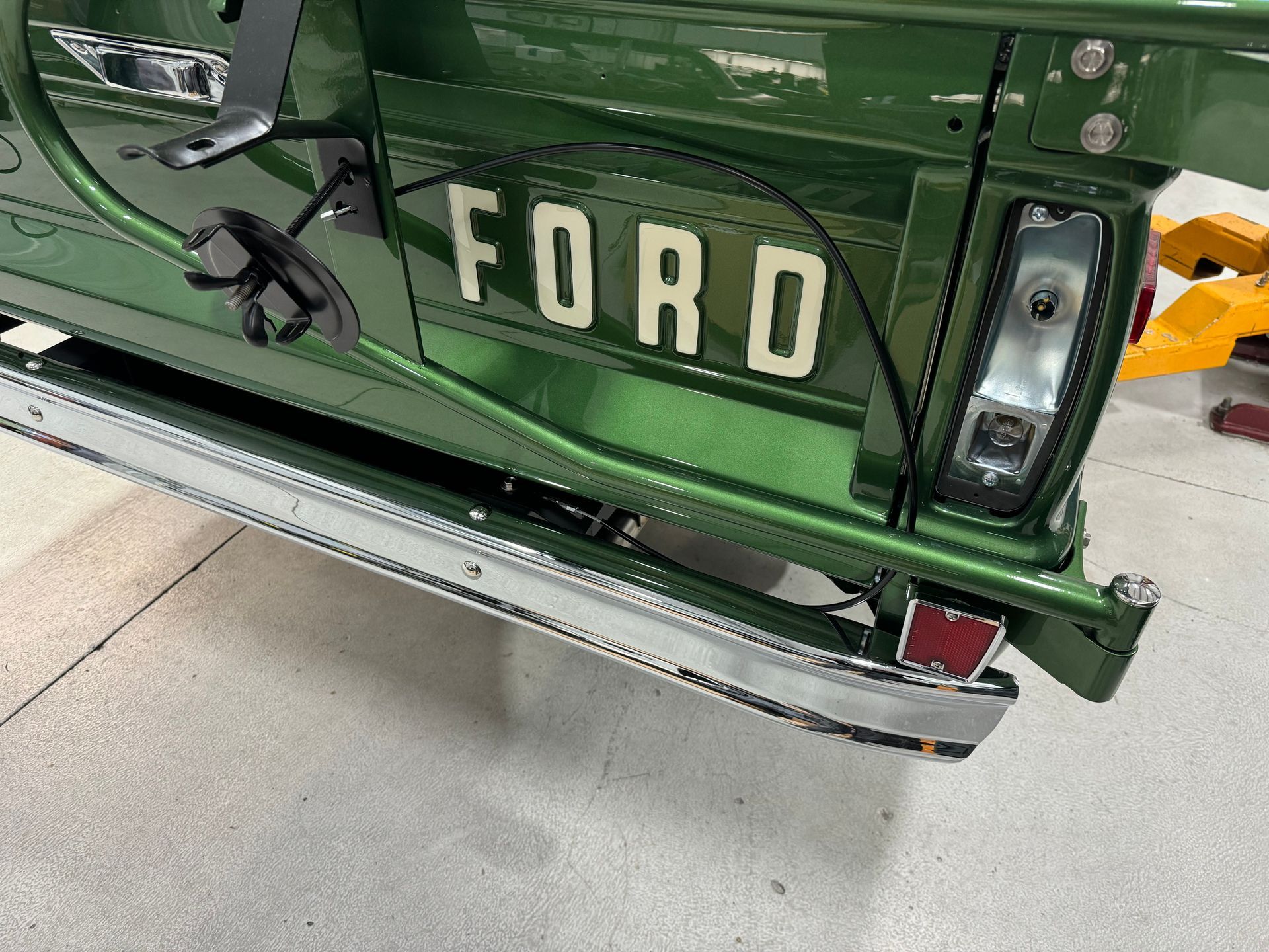 Close-up of a green Ford truck tailgate with white lettering and chrome bumper in a garage.