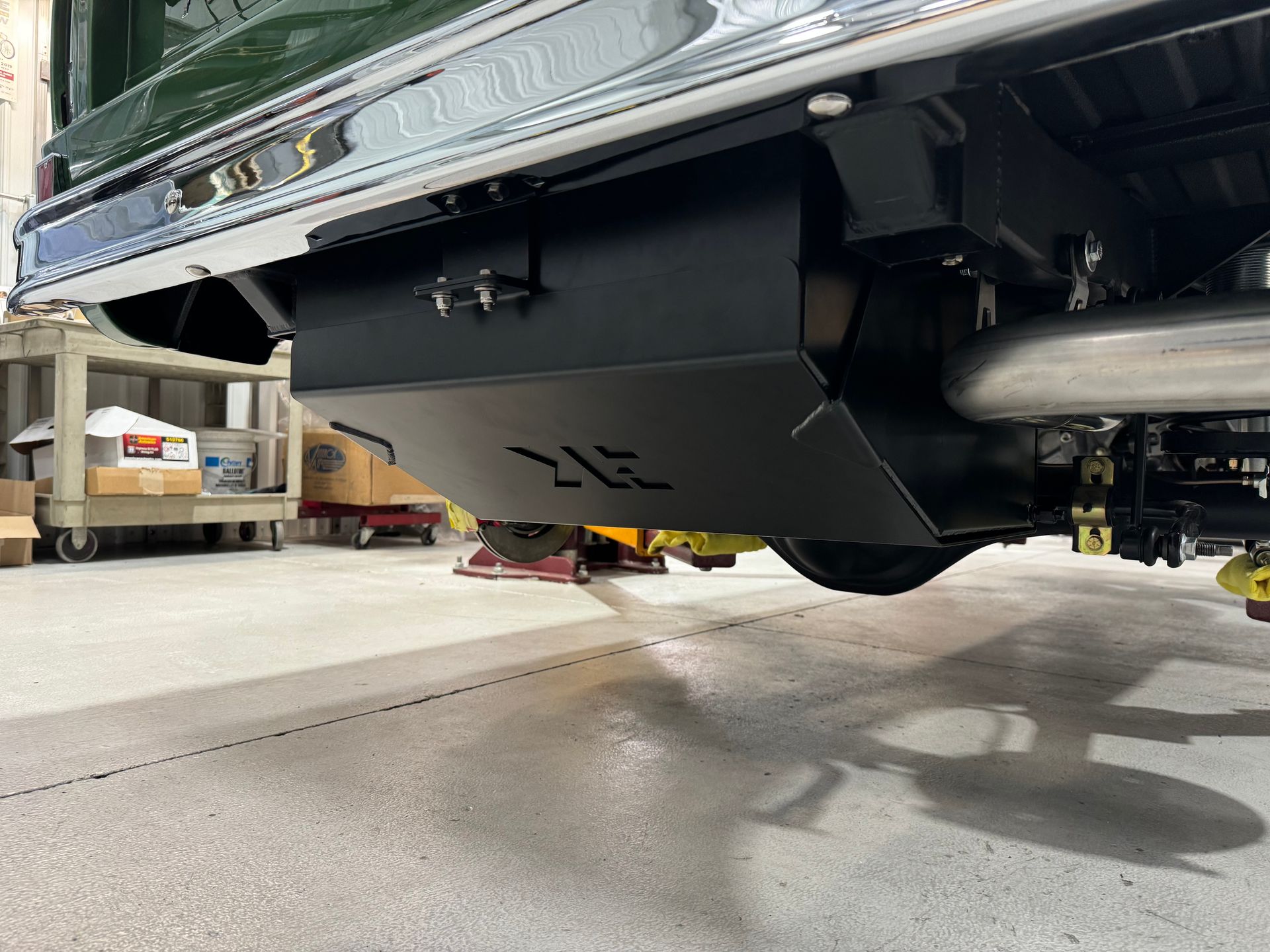 Black metal box mounted under a car, viewed from the rear in a garage.