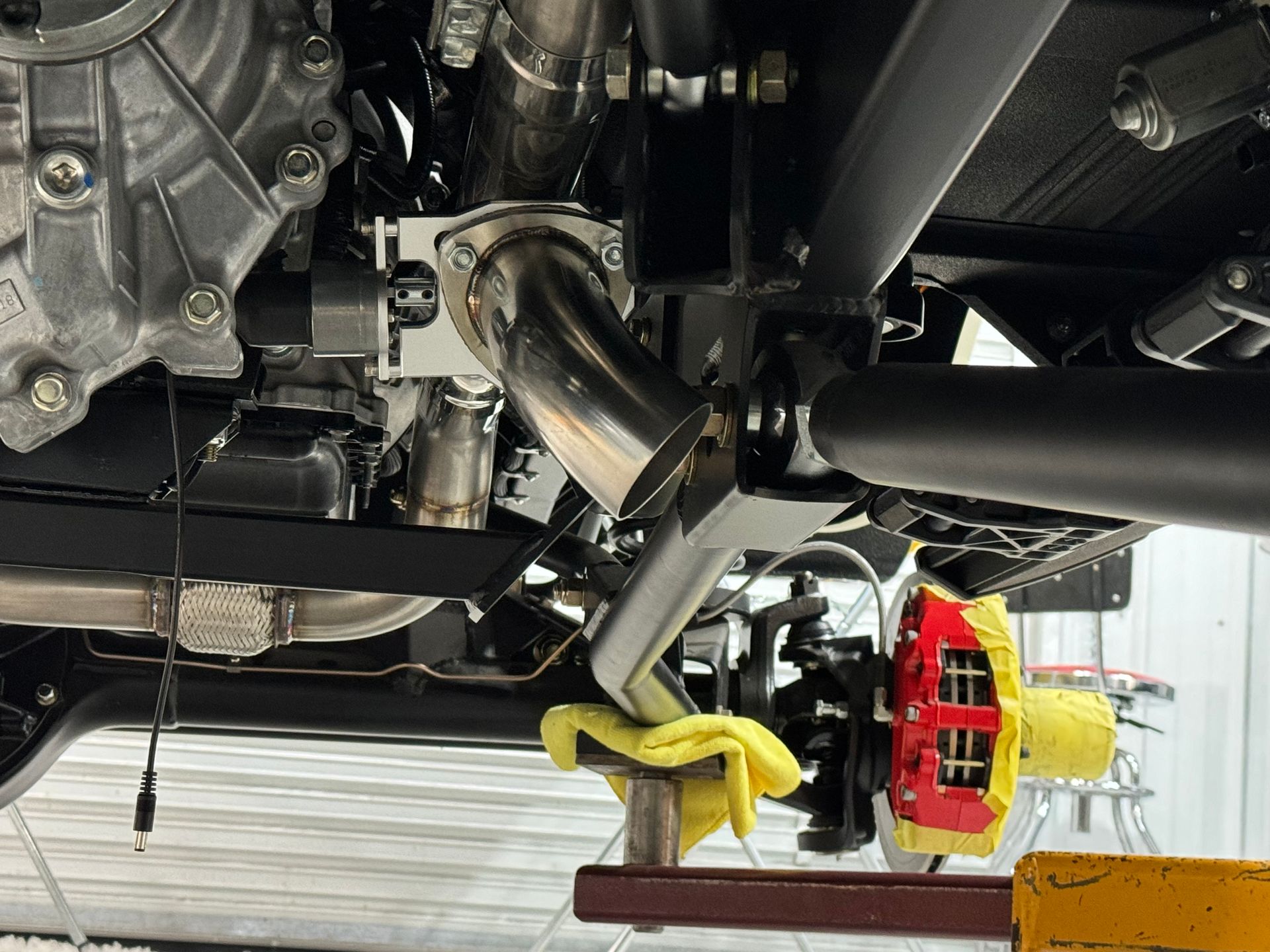 Undercarriage of a vehicle on a lift, showing exhaust piping and a yellow brake caliper.