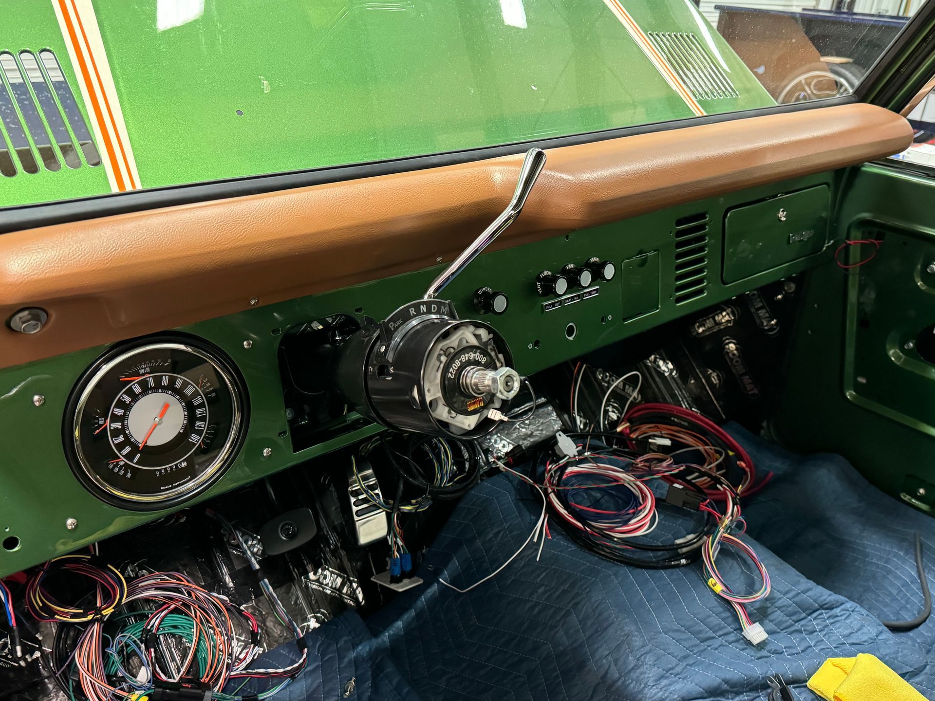 Car dashboard interior with exposed wiring, gauges, and a steering column on a blue floor mat.