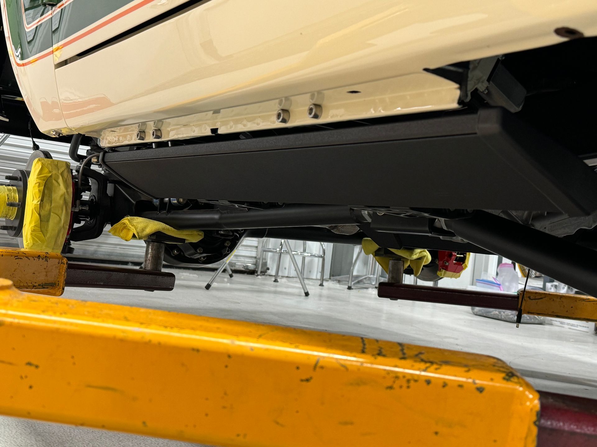 Undercarriage of a boat on a lift, with yellow supports and a black hull panel in a workshop.